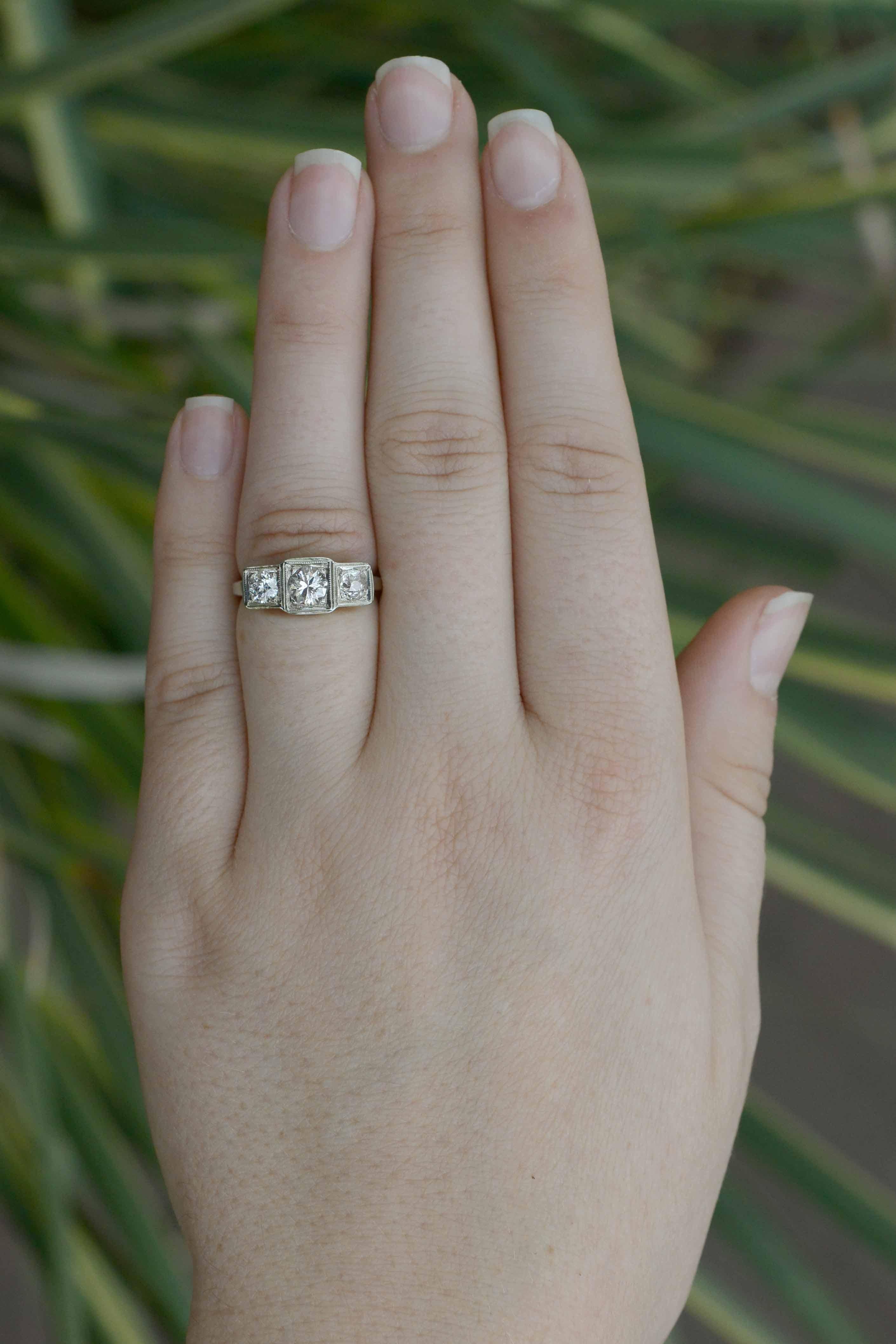 A 14k white gold 3-stone antique diamond engagement ring featuring classic Art Deco style architecture in the under gallery. Set with 0.90 carats total of glittering and fiery old cut diamonds tastefully set with tiny bead prongs, each of the gems