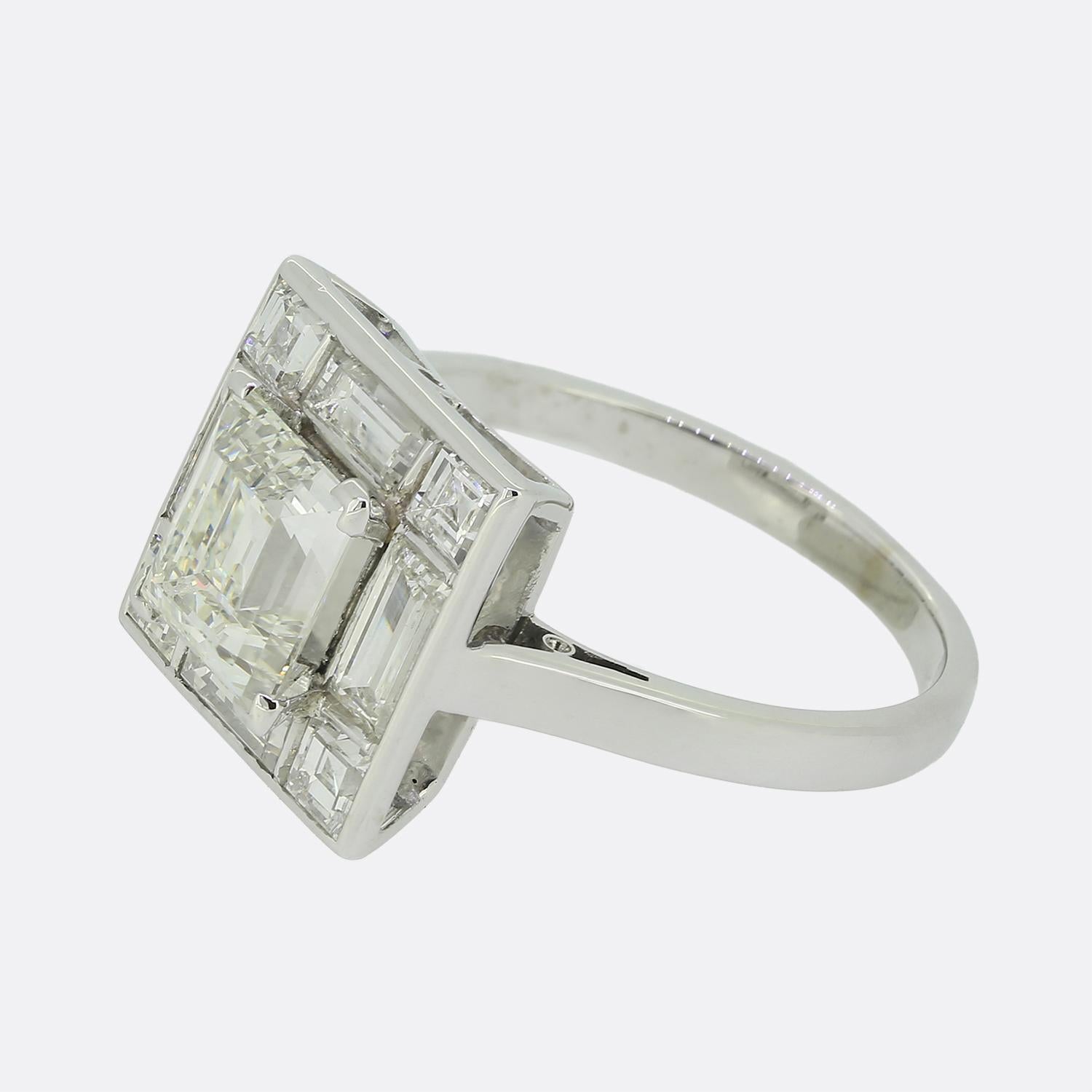 Here we have an exquisite Art Deco cluster ring featuring a captivating square shaped diamond at the centre of the face. This principal stone sits slightly risen in a four-clawed setting atop a backdrop consisting of smaller matching square stones