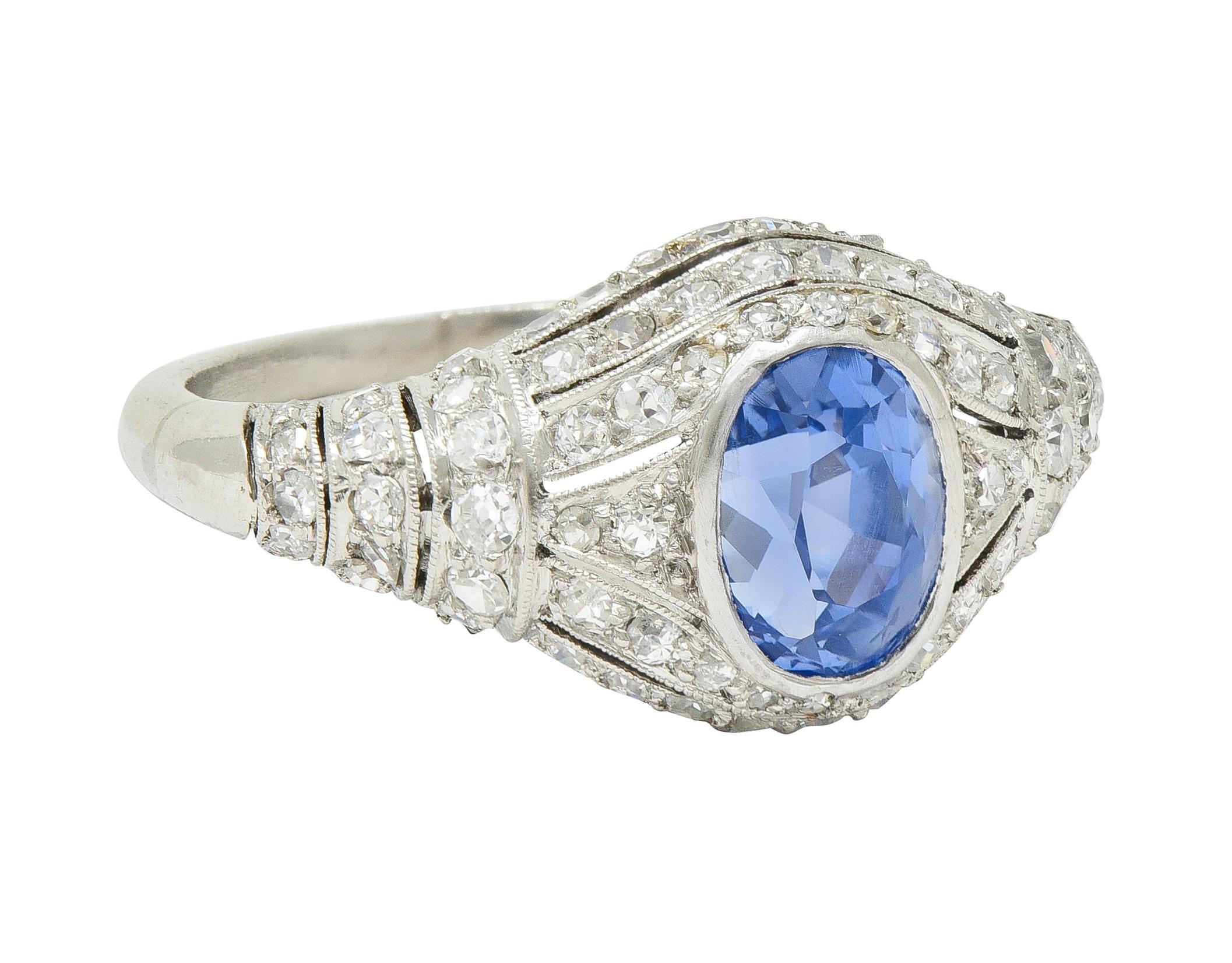 Centering an oval-shaped mixed-cut sapphire weighing 1.70 carats - transparent cornflower blue in color 
Natural Sri Lankan in origin with no indications of heat treatment - bezel set
With a pierced bombé-shaped surround with rows of single cut
