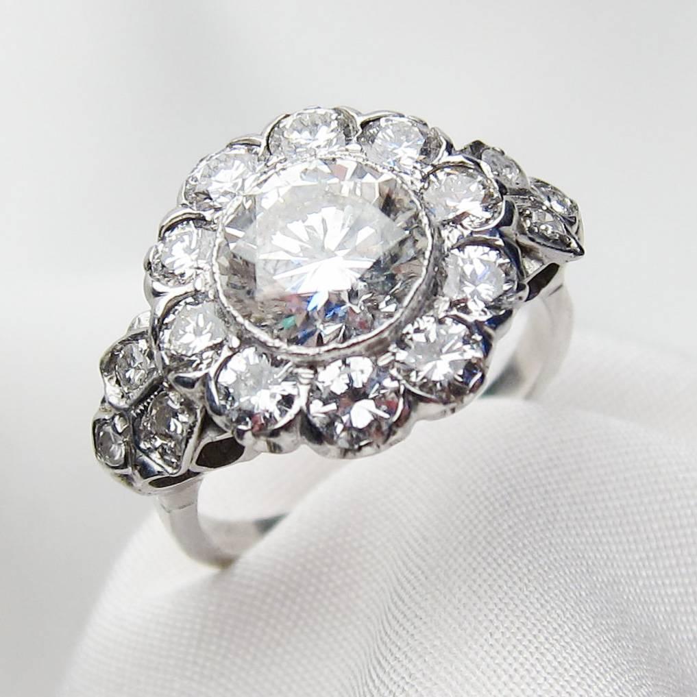 Circa 1930. This elegant Art Deco 18KT white gold halo ring features a fantastic central bezel-set, brilliant-cut diamond, weighing 1.97 carats, with an SI3 clarity and H color. Accenting the central gem is a lovely halo of 10 bead-set,