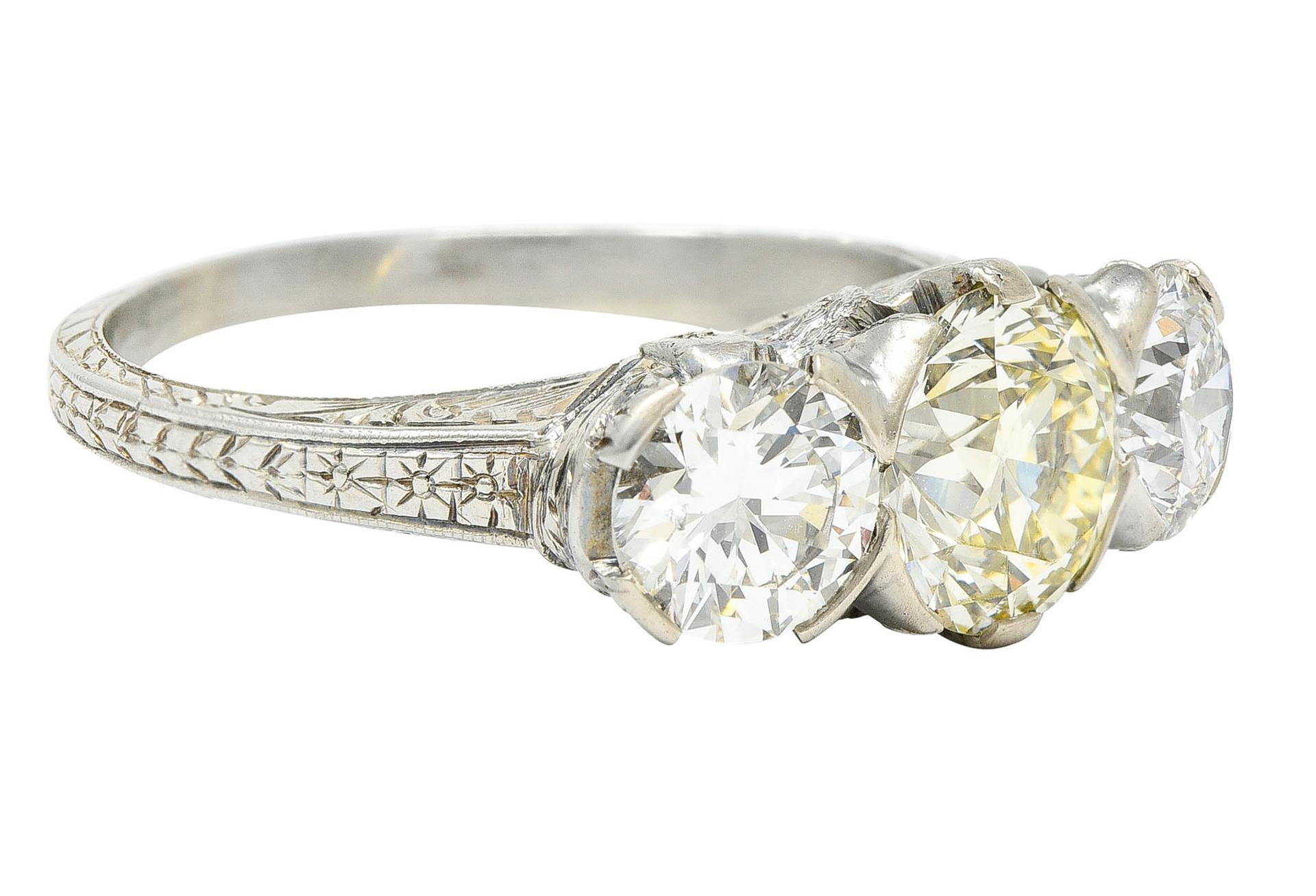 Three stone ring centers a light yellow diamond weighing 1.64 carats - uniform in color with VS clarity

Flanked by two transitional cut diamonds weighing in total approximately 1.56 carats - G/H color with VS and SI clarity

Set by wide decorative