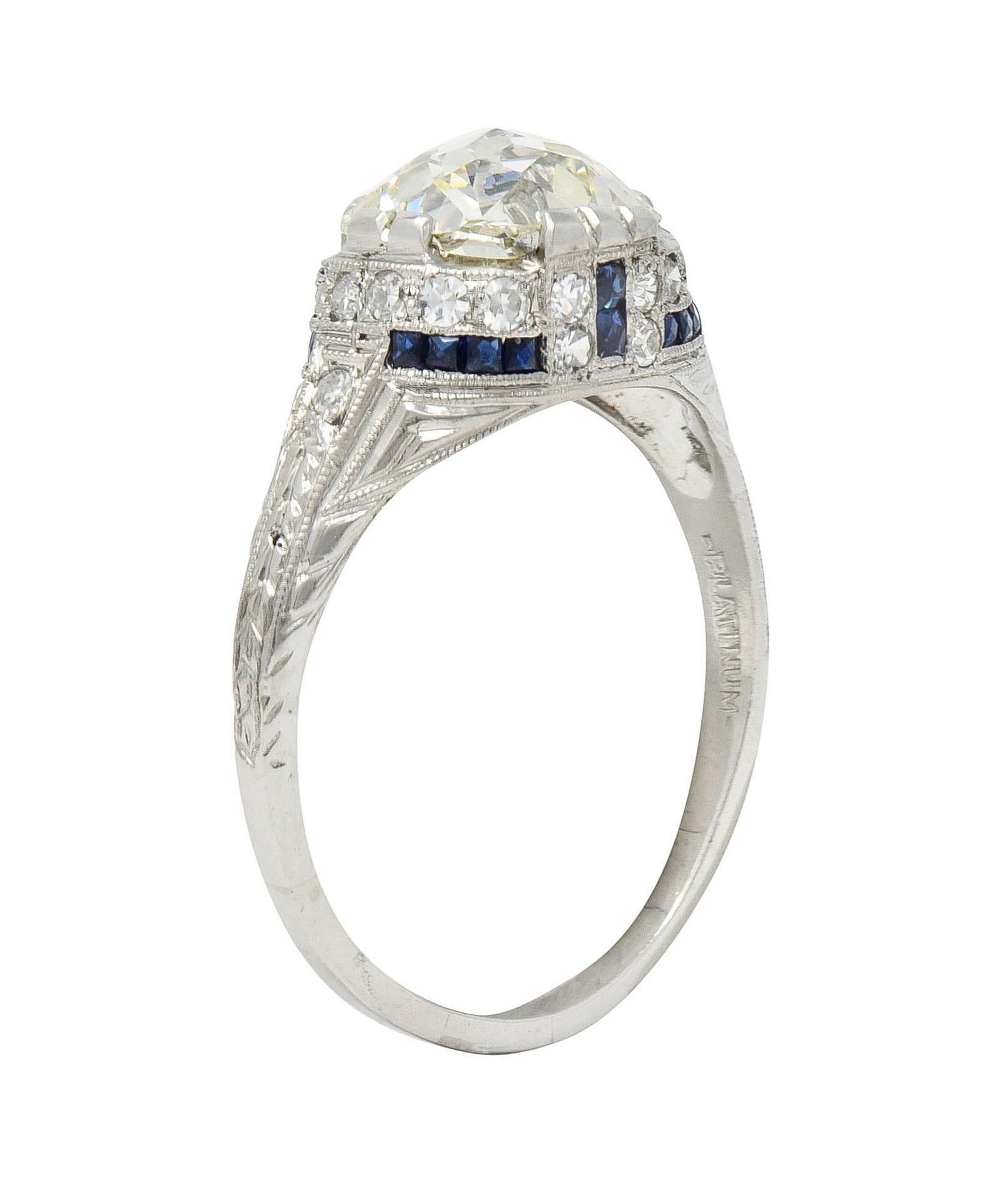Centering a Jubilee cut diamond weighing 2.59 carats - N color with VS2 clarity
Set with split tab-like prongs with a milgrain detailed geometric motif gallery 
Channel set with rows of transparent medium blue French cut sapphires 
Weighing