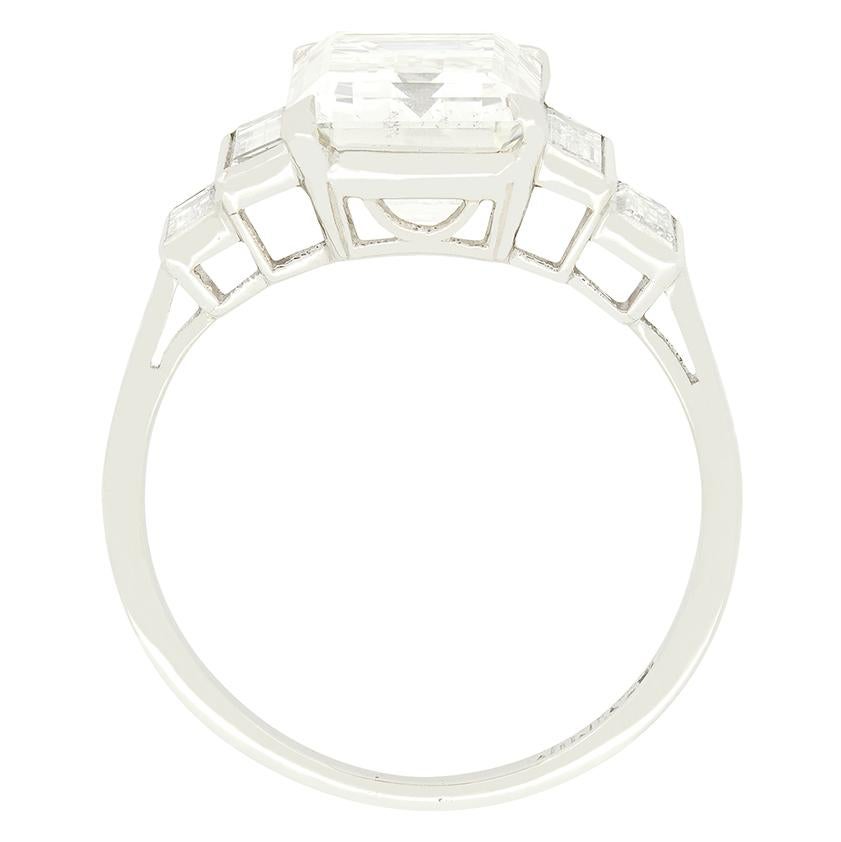 With an impressive emerald cut diamond at its heart, this beautiful solitaire ring dates to the 1920s. The central diamond is 3.29 carat in weight with a colour of J to K and clarity of VS2. Set within a platinum collet the diamond is flanked by