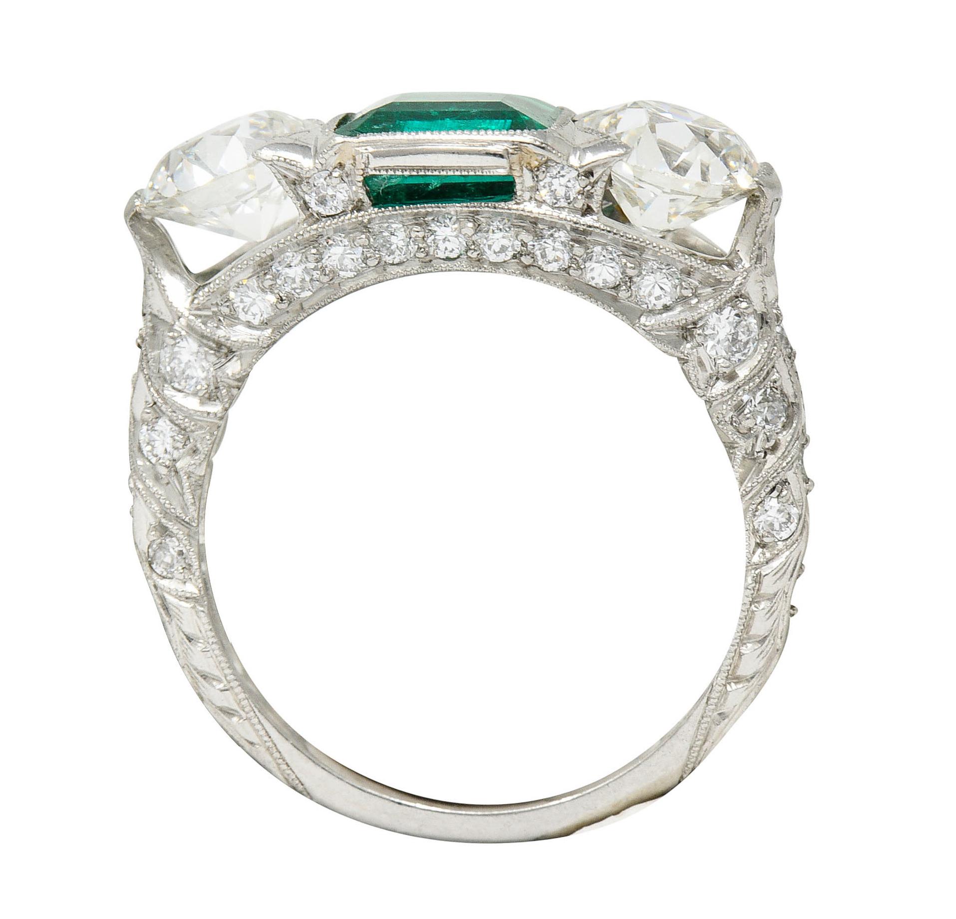 Designed as a three stone ring with ribbon motif shoulders and milgrain edges

Centering a square cut emerald weighing approximately 1.20 carat - transparent with bright green color

Flanked by two old European cut diamonds weighing in total