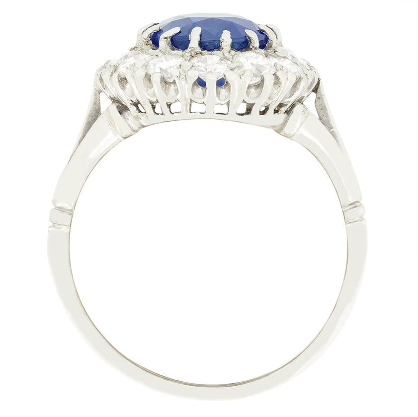 Dieser atemberaubende Clusterring stammt aus den 1920er Jahren. Sein Herzstück ist ein beeindruckender, intensiv blauer Saphir von 3,50 Karat. Der Saphir ist ein natürlicher, erhitzter Stein, geschliffen in einer alten ovalen Form, gefasst in