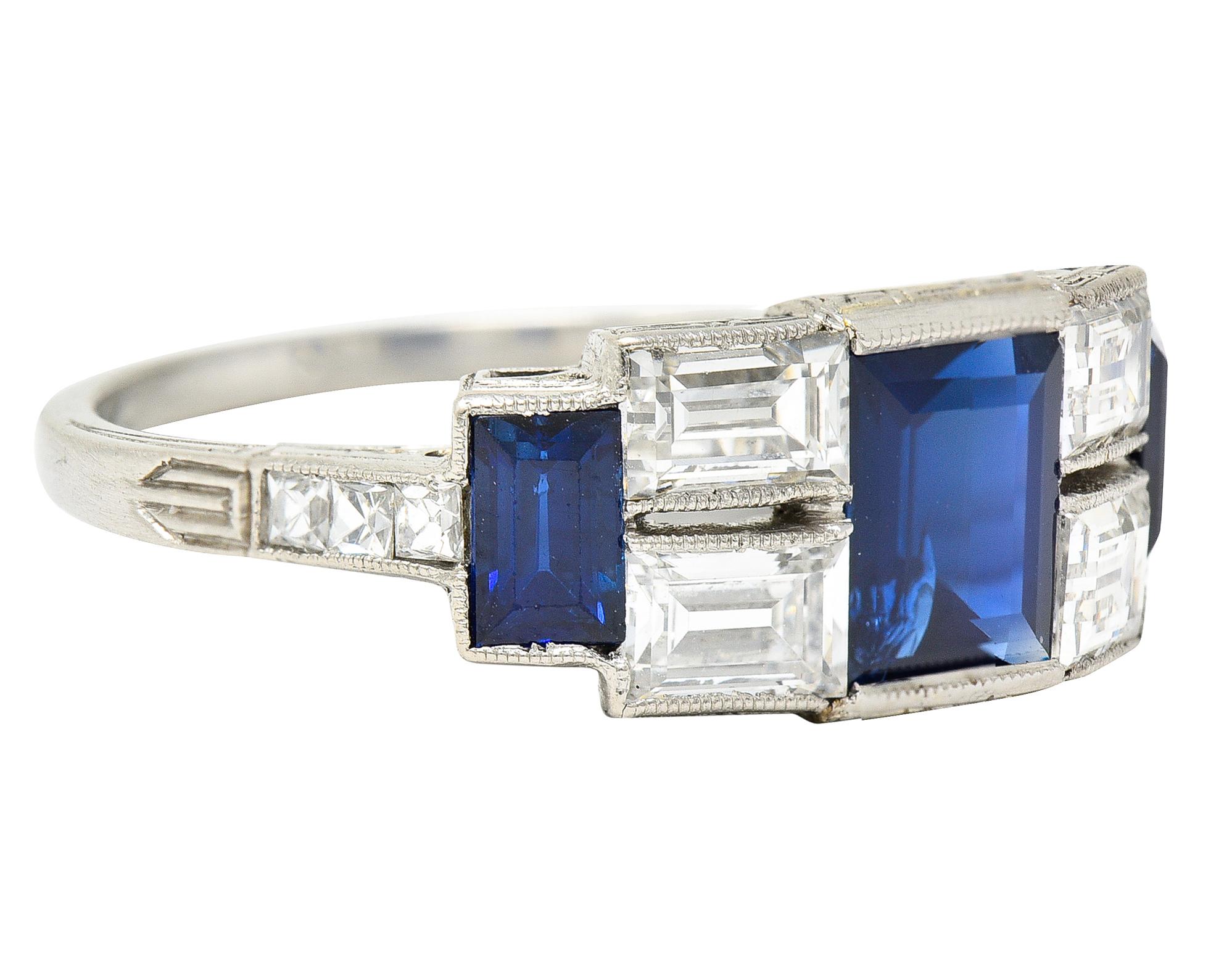 East to West band ring features sapphire and rectangular step cut diamonds. With channel set French cut diamonds at shoulders accented by linear engraving. Sapphires are transparent and well matched in royal blue color while weighing 1.25 carats