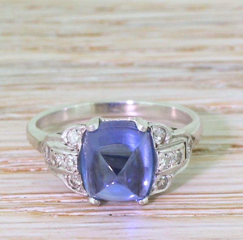 A hypnotically beautiful natural, no-heat sugarloaf sapphire ring. The glowing centre stone bullet-shape (or sugarloaf) cabochon sapphire holds an almost magical glow; internally clean and impressively bright. The sapphire is secured in a four-claw