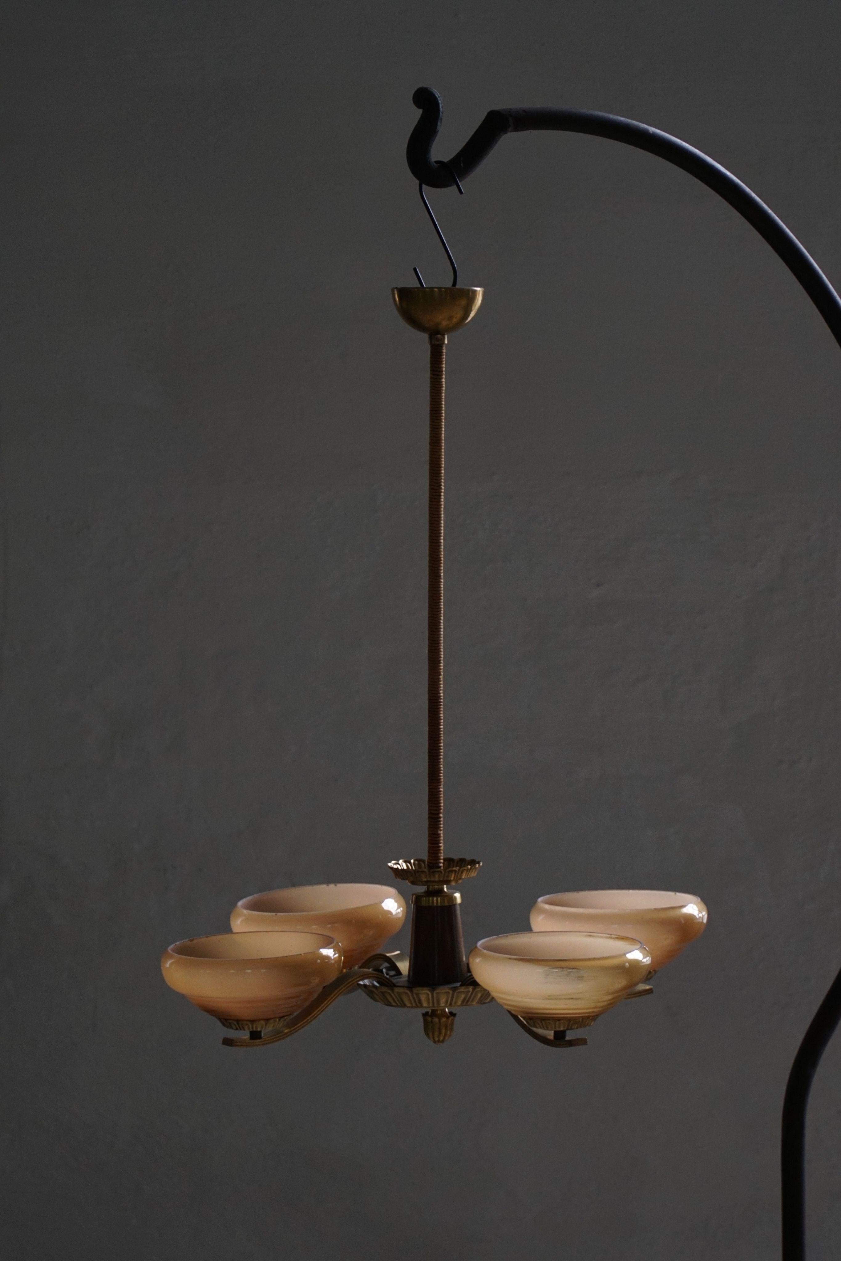 Ce lustre exquis à 4 branches incarne l'élégance et le savoir-faire du design Art déco suédois des années 1940. Avec ses bras doucement courbés en laiton finement vieilli, chacune supporte un abat-jour en verre délicatement teinté dans des tons