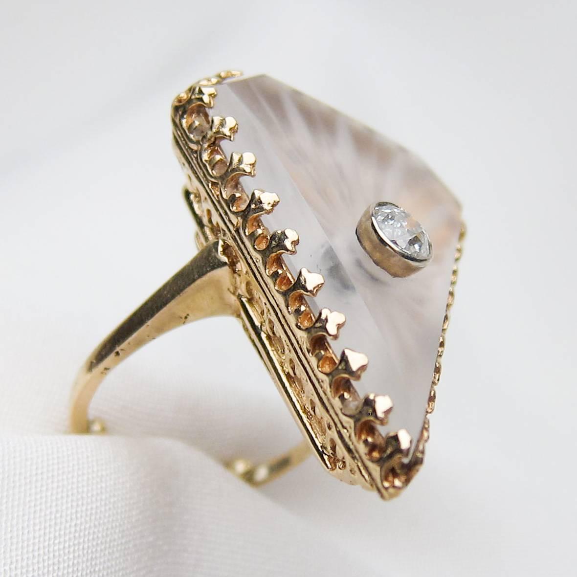 This is a fabulous rock crystal ring from the 1920s set in 14KT yellow gold and platinum. The mounting features a fleur-de-lis motif encircling a shield-shaped slice of rock crystal. In the center of the crystal sits a bezel-set old European-cut