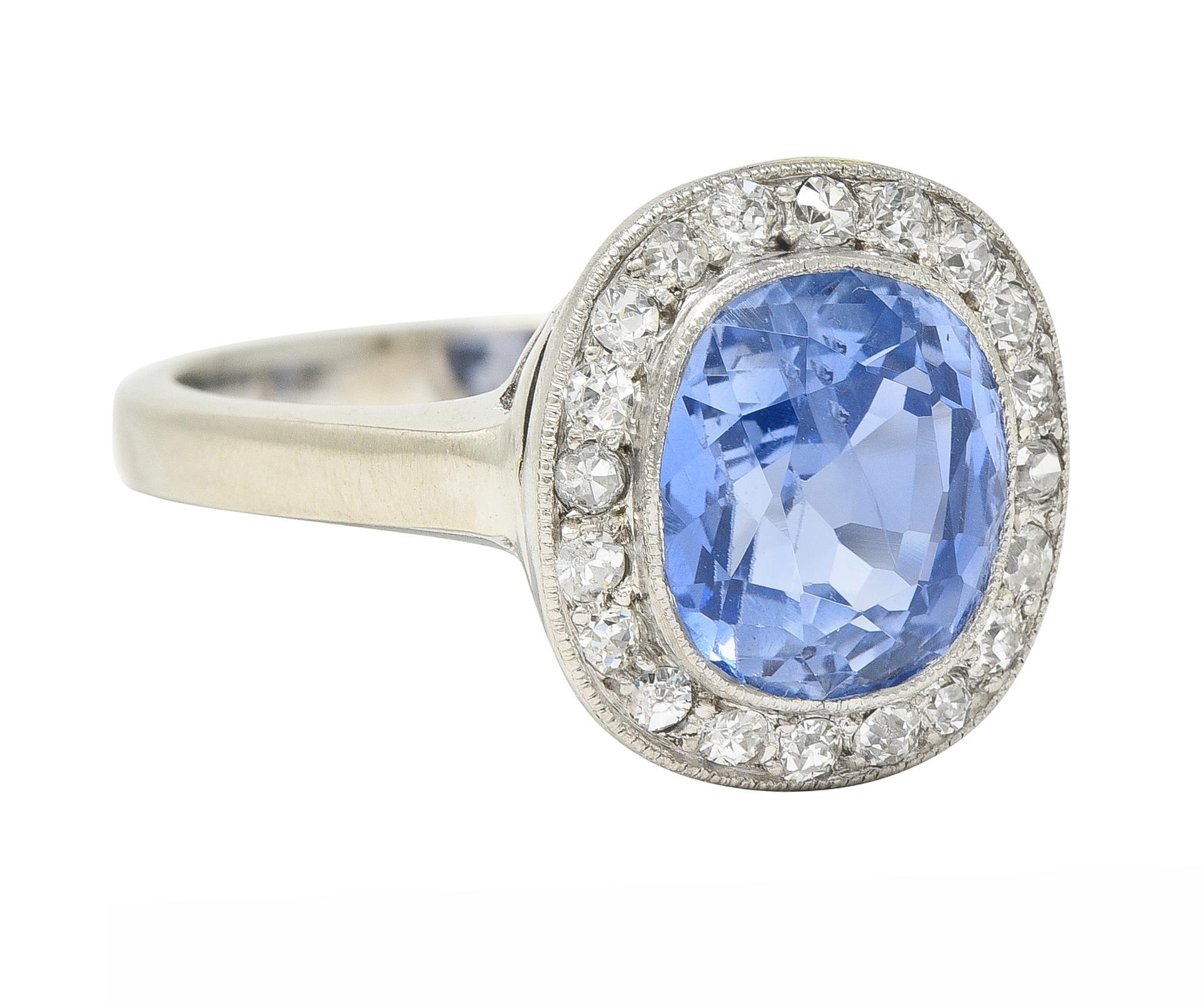 Centering a cushion cut sapphire weighing 3.61 carats - transparent medium blue in color 
Natural Sri Lankan in origin with no indications of heat treatment - bezel set
Featuring a halo surround of bead set old European cut diamonds 
G/H in color
