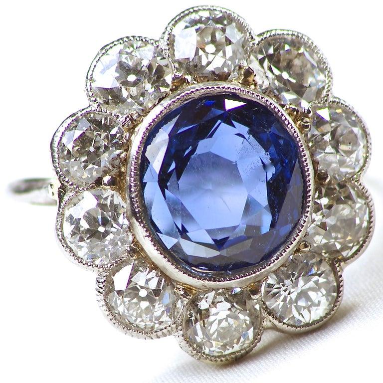 This iconic Art Deco cluster ring features a 4.82 carat Burma no heat sapphire displaying a deep vivid blue color. A rare color that is sought after and admired by proud owners and guests. Surrounded by pedals of old cut near colorless diamonds. The