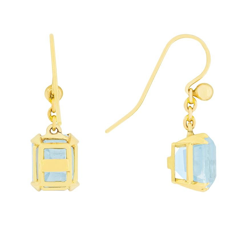 Two powder blue aquamarines are suspended in these art deco earrings. The aquamarines are 2.50 carat each, and are emerald cut. They are claw set in the 18 carat yellow gold, which extends to the earring back. The contrast of the blue aquamarines