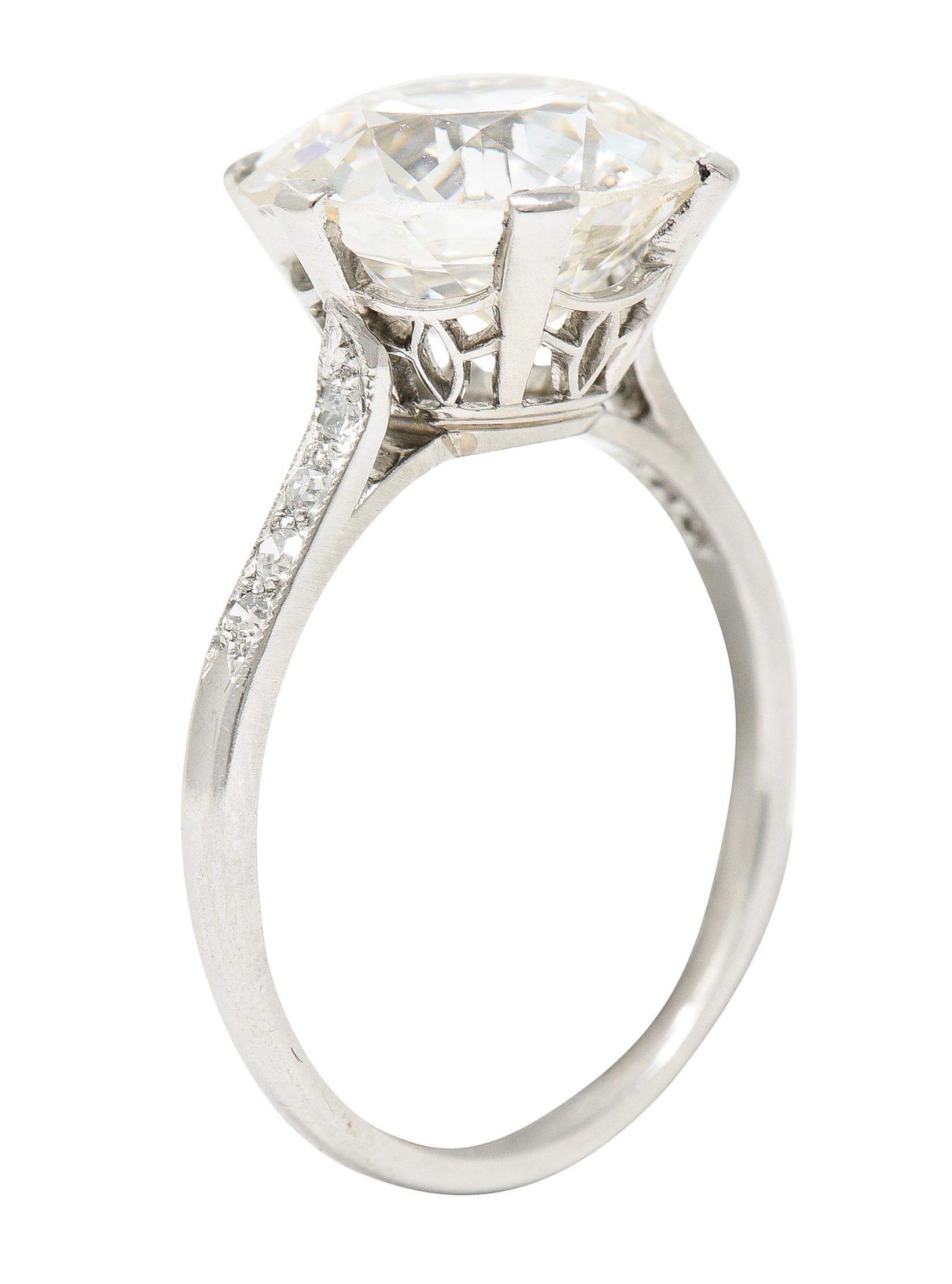 Centering an old European cut diamond weighing 4.99 carats total - J color with VS2 clarity. Set in a six prong basket - pierced with geometric foliate motif. Flanked by tapered cathedral shoulders. Bead set with single cut diamonds. Weighing