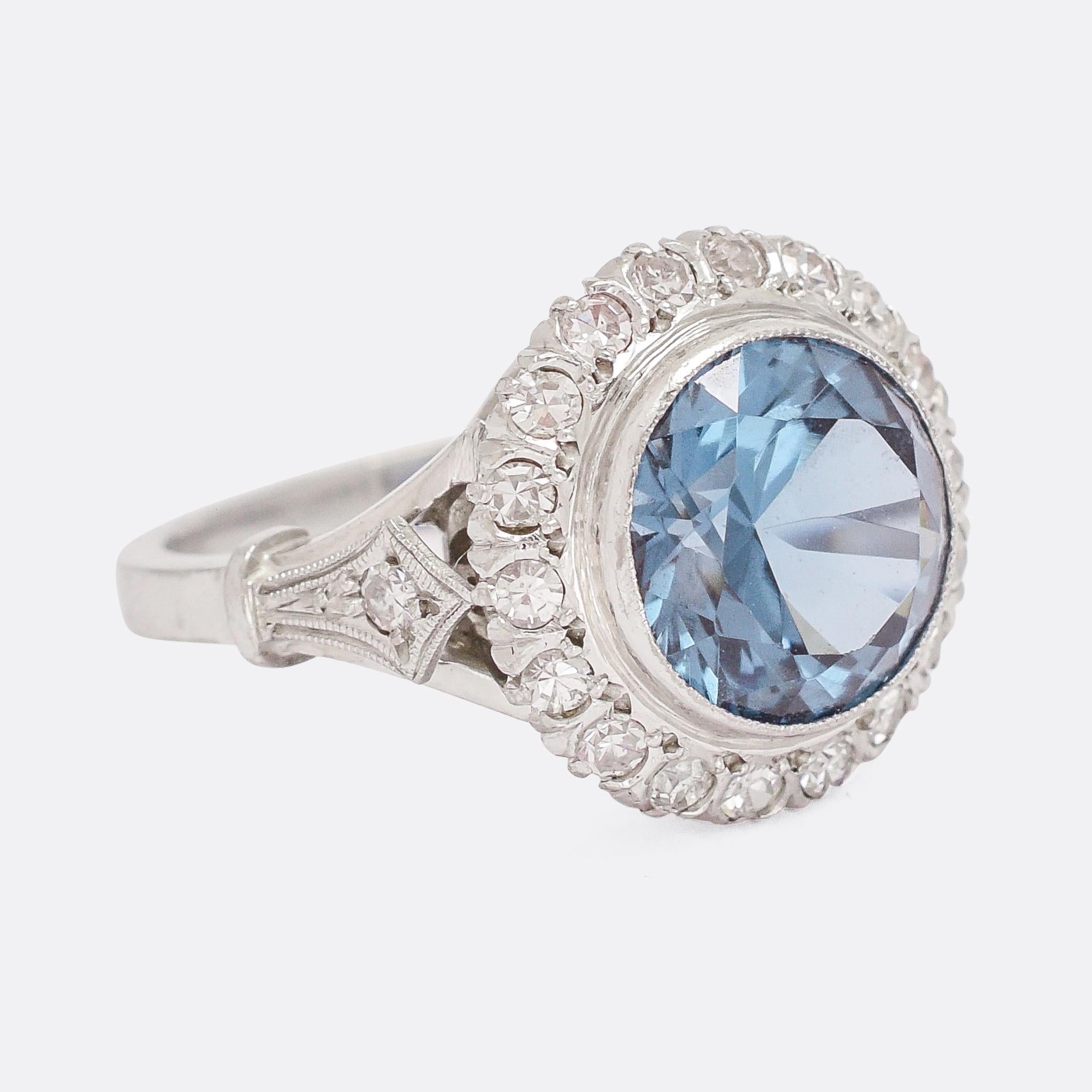 A wonderful Art Deco cocktail ring set with a juicy 5.2ct blue zircon surrounded by a ring of fine millegrain and a halo of diamonds. The styling is very typically deco, with diamond millegrain shoulder accents and crafted in platinum throughout. A