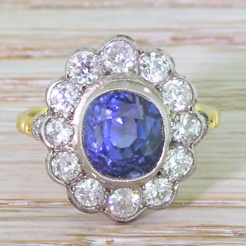 Supremely beautifully. The gorgeous and glowing natural Ceylon sapphire is the perfect cornflower blue with bright flashes of indigo. Rubover and milgrain set, the sapphire is surrounded by twelve high white old European cut diamonds atop simple,