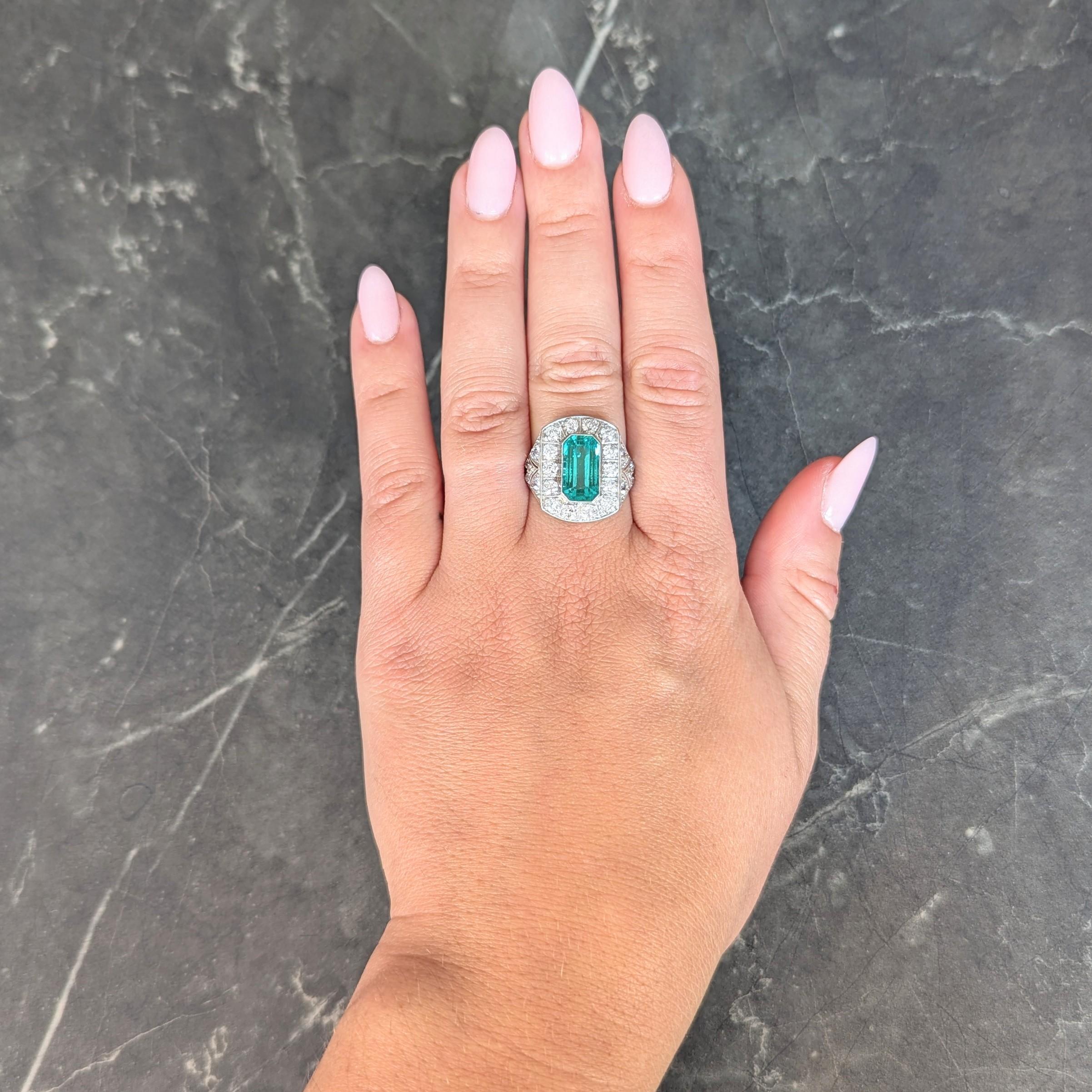 Centering an elongated emerald cut emerald weighing 4.02 carats total
Natural Colombian in origin with minor clarity enhancement (F1)
Transparent light green in color - bezel set with halo surround
Cushion-shaped and bead set with old European cut