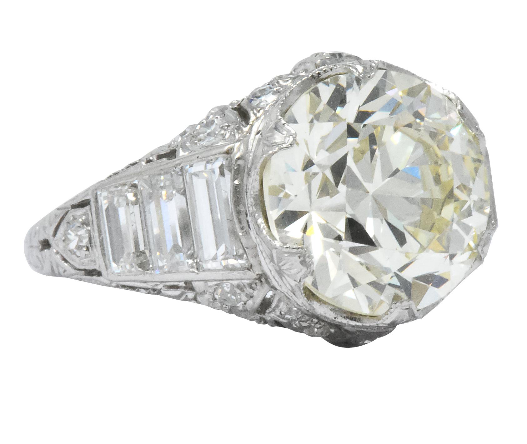Centering a transitional cut diamond weighing 4.66 carats; O to P color with VS2 clarity

Ornately set with stylized scalloped prongs accented by milgrain and a hand engraved burst motif 

Flanked by channel set baguette cut diamonds and set