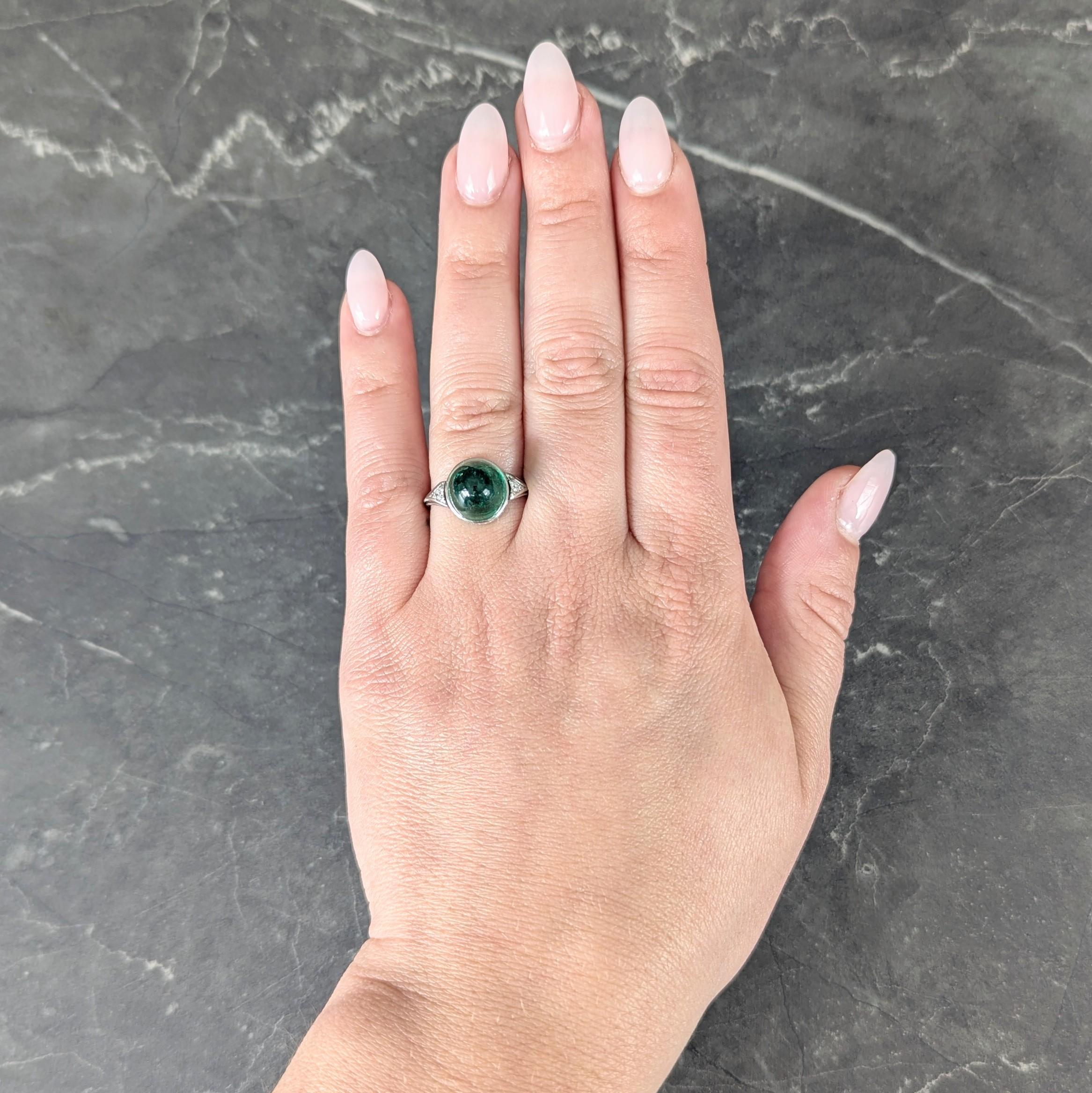 Centering a round bullet shaped cabochon weighing 6.26 carats - transparent medium green in color
Natural Colombian in origin displaying minor traditional treatment and bezel set
Engraved with a scroll motif profile and flanked by old European cut