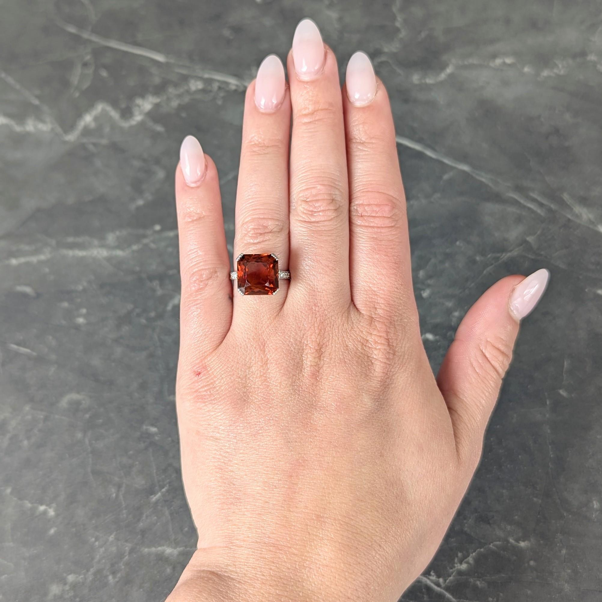 Centering a mixed square cut citrine weighing approximately 7.02 carats -
Transparent deep brownish orange - set with grooved prongs
In a pierced geometric and scallop motif basket
Accented by a bead set hidden halo of diamonds
With additional