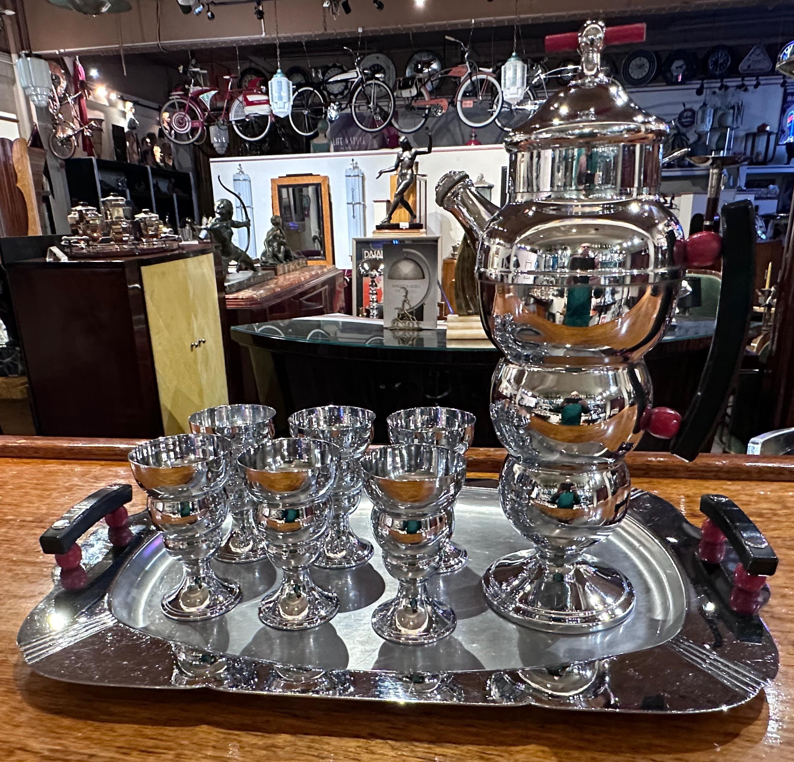 Art Deco 8-piece chrome “Bubble” cocktail shaker set designed by Omer A. Menard in 1935 for Farberware, Brooklyn, NY. The shaker with three graduated spheres on a ring foot with a pour spout and curved black handle with red ball spacers all topped