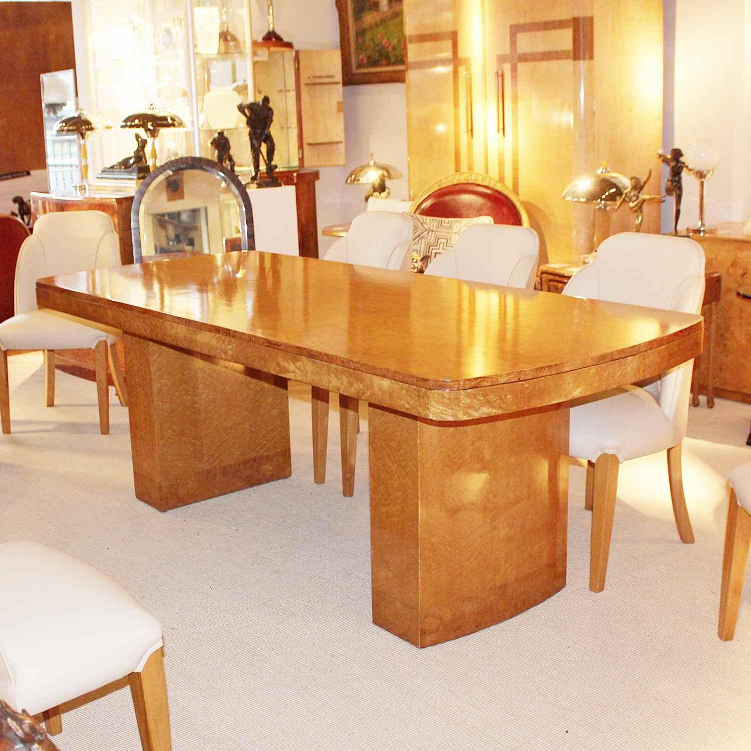 An Art Deco dining table with eight chairs. Table set over curved pedestals. Cloud form chairs upholstered in cream leather and Alcantara suede. Figured bird's-eye maple throughout. 





 