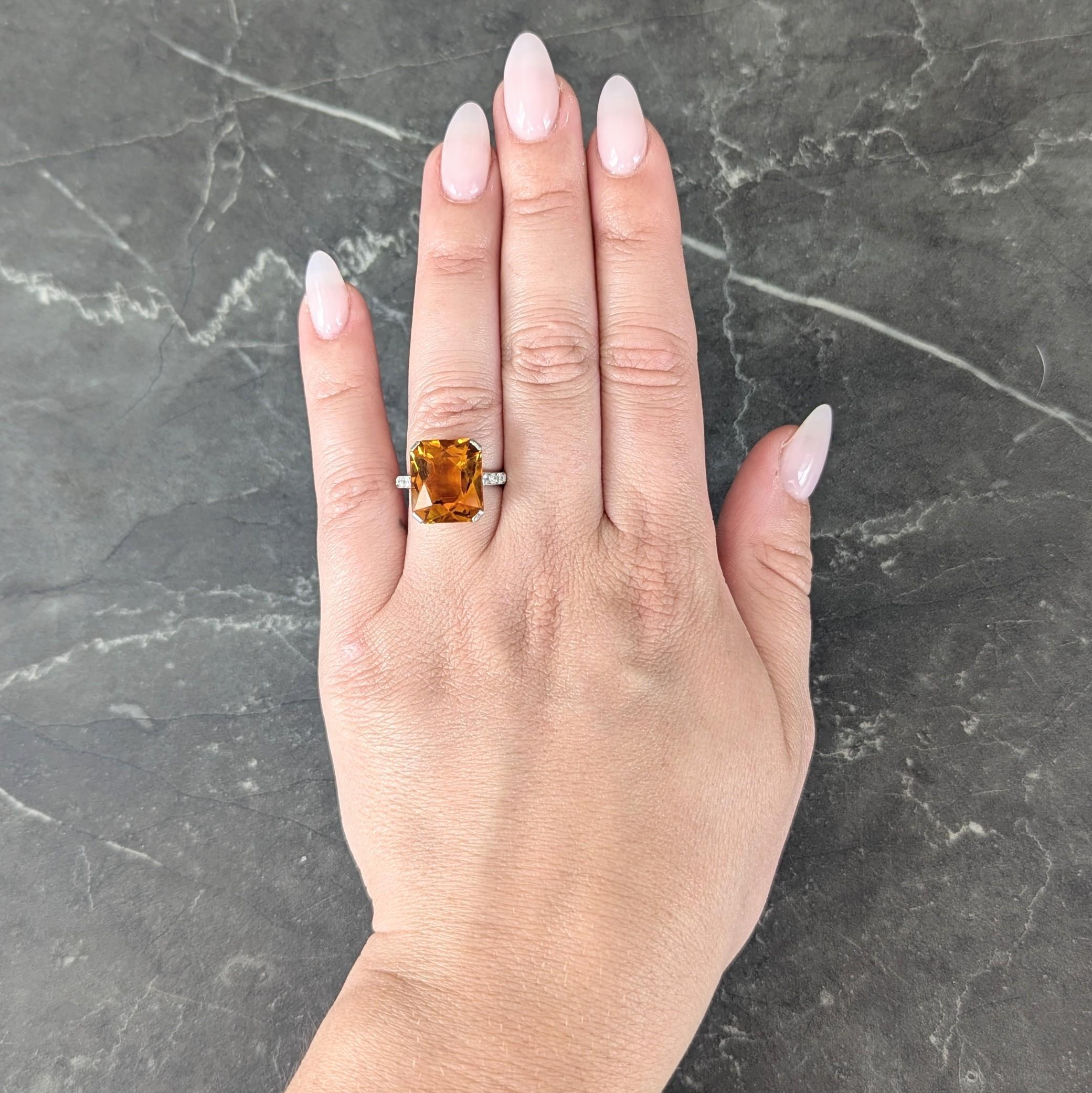 Centering a radiant cut citrine weighing approximately 8.77 carats
Transparent medium brownish orange with light striations in color
Set in basket via corner tab prongs and flanked by cathedral shoulders
Bead set with transitional cut diamonds in