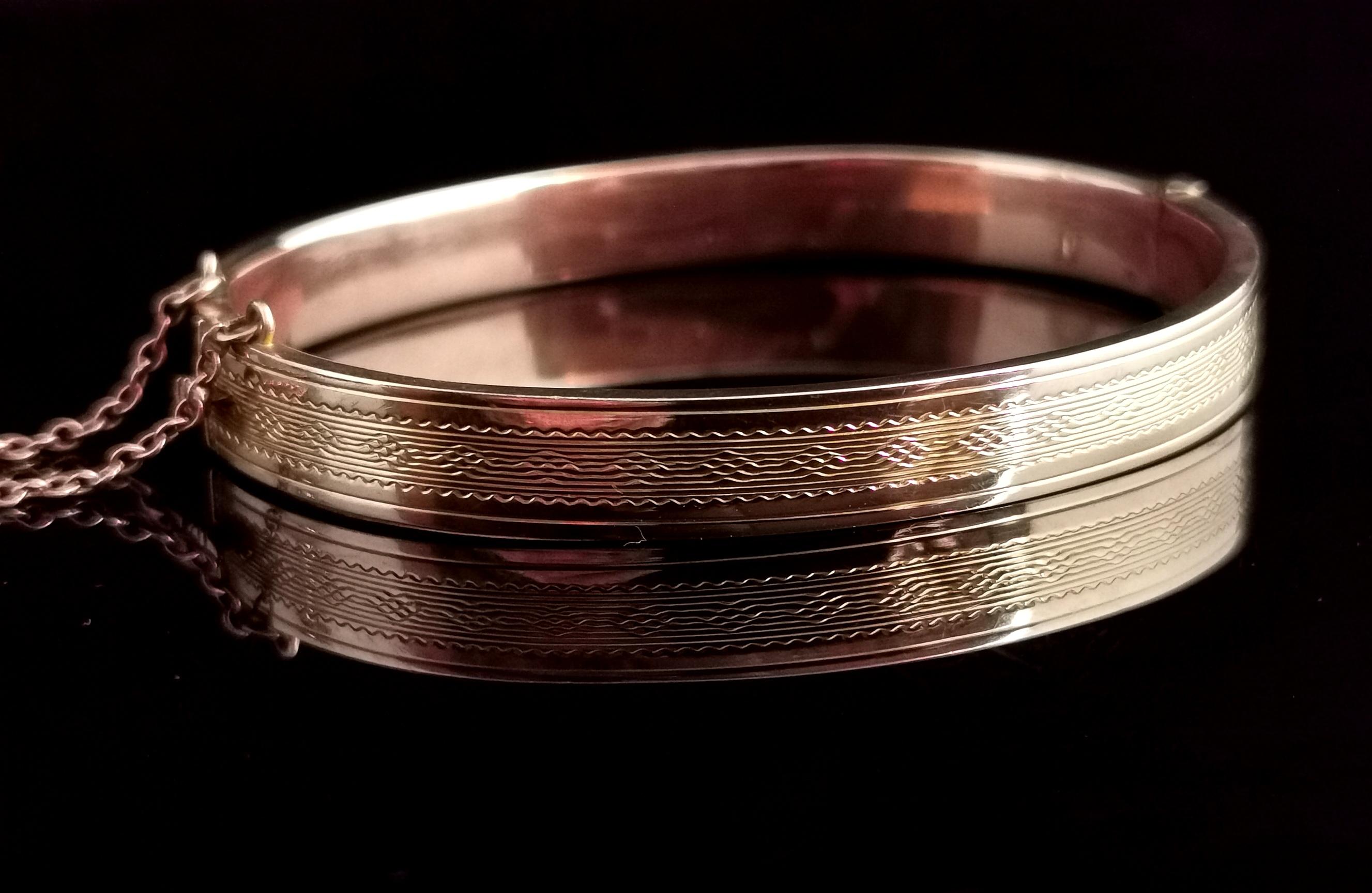 A beautiful vintage Art Deco era 9kt Rose gold bangle.

It has an attractive engine turned half design with slight yellow gold highlights within the engraving.

The reverse of the bangle is a smooth polished finish and it has a push catch and safety