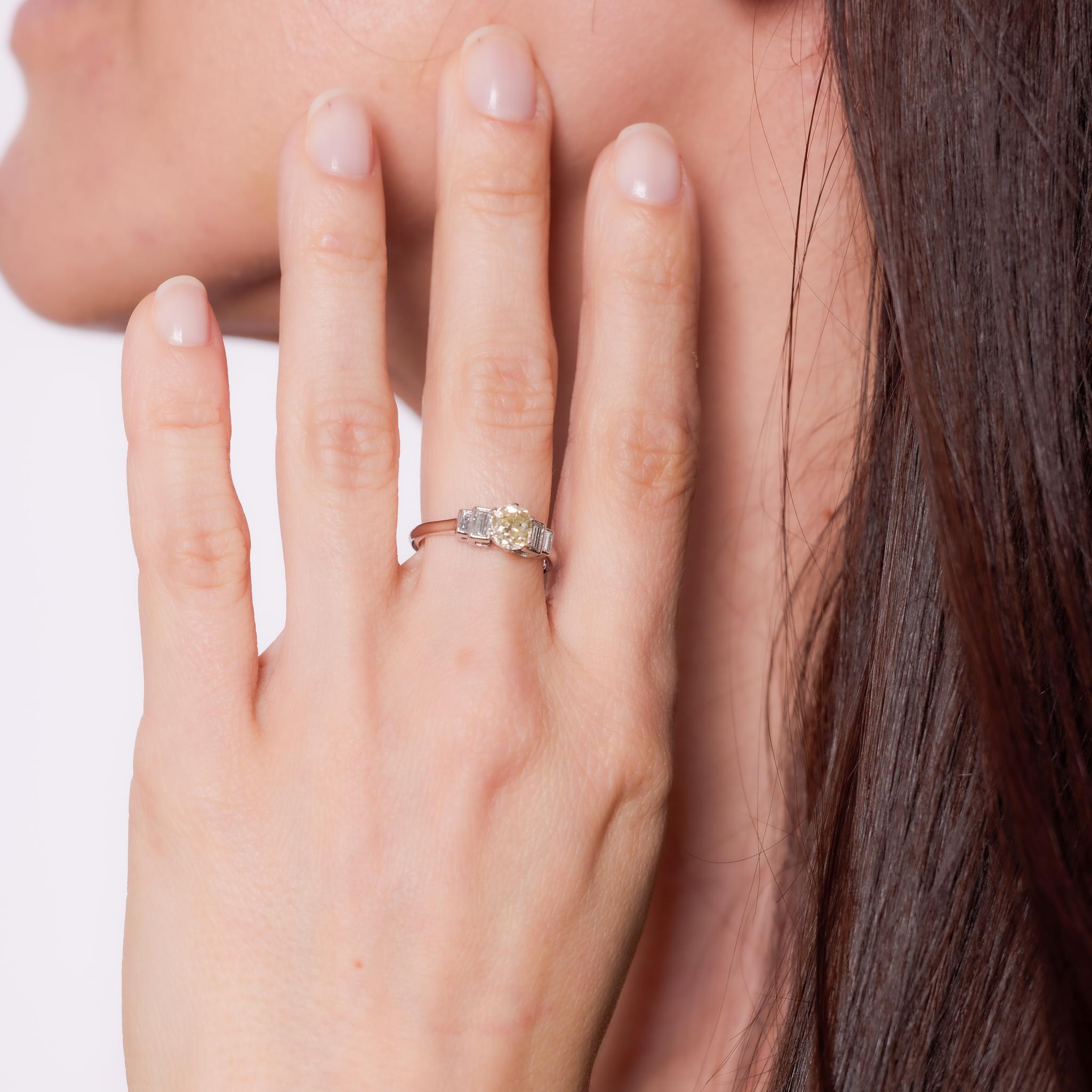 Crafted in the 1930s, this Art Deco engagement ring is set in platinum and showcases an old mine cut diamond weighing approximately .90 carats, graded U-V light yellow and SI1 clarity. Four baguette cut diamonds totaling approximately .20 carats,