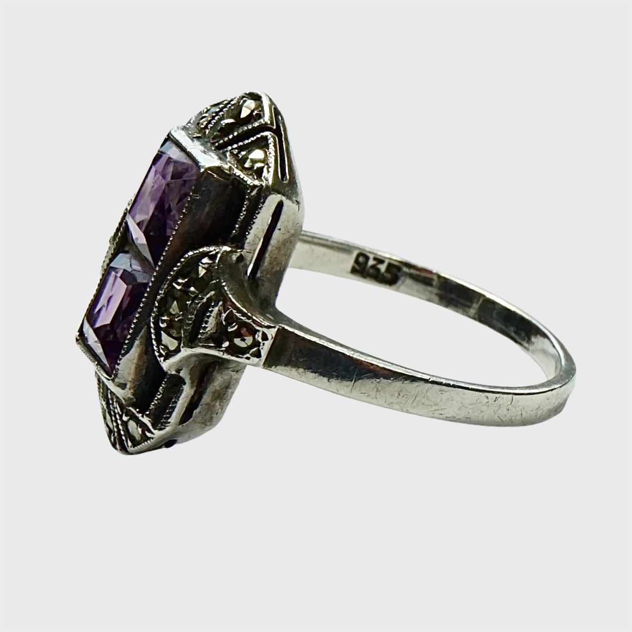 Beautiful Art Deco 935 silver ring set with marcasites and two faux amethyst stones. Ring size UK M / US 6, inside diameter 1.7 cm / .67 inch. The front measures length 1.8 cm / .7 inch. The band is at a slight angle, this is most likely how it was