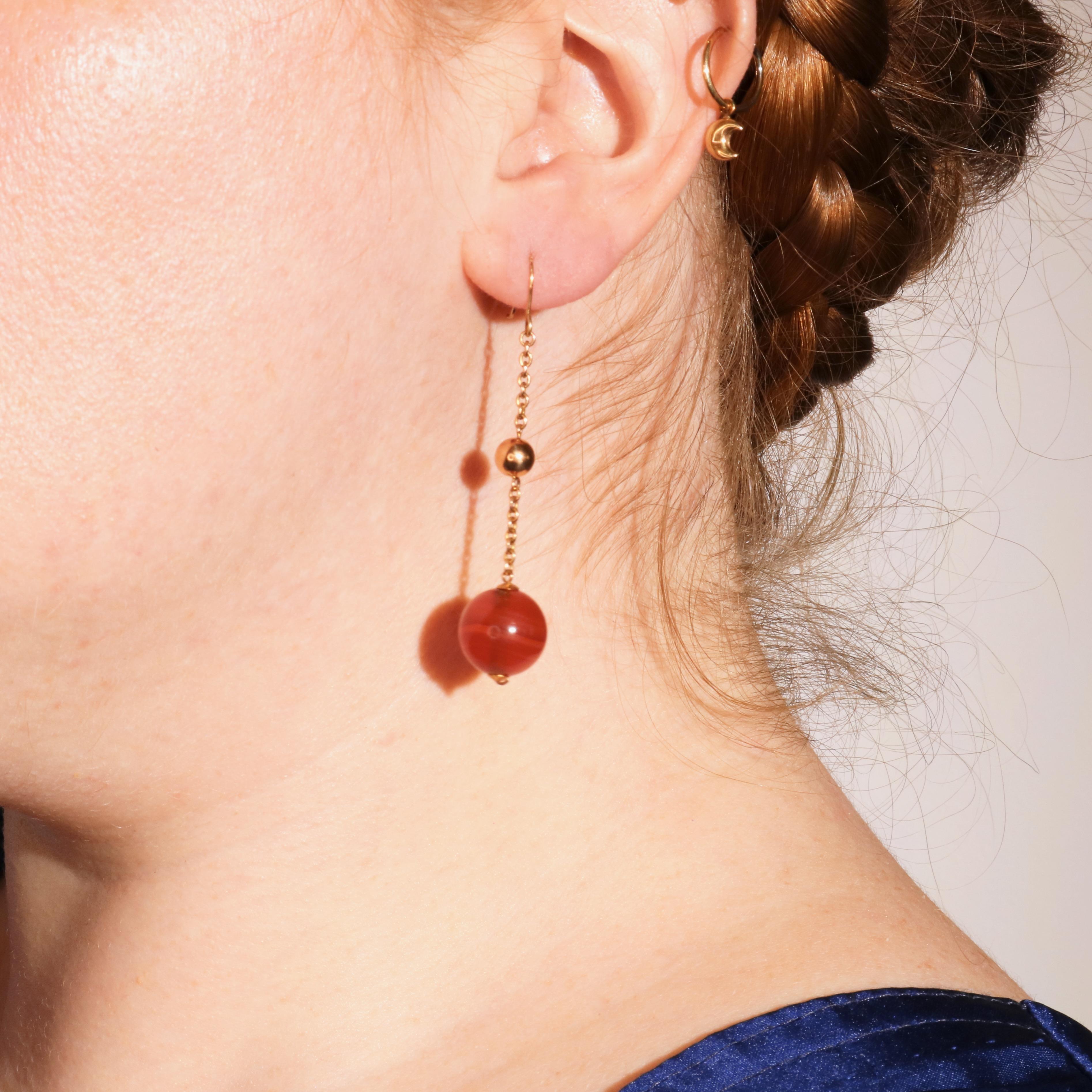 A pair of earrings in yellow gold, each comprising one spherical carnelian cabochon, set to 9 karat yellow gold drops, complete with 9 karat yellow gold hook backs. 

Each earring is set with a spherical carnelian cabochon. The spheres of carnelian
