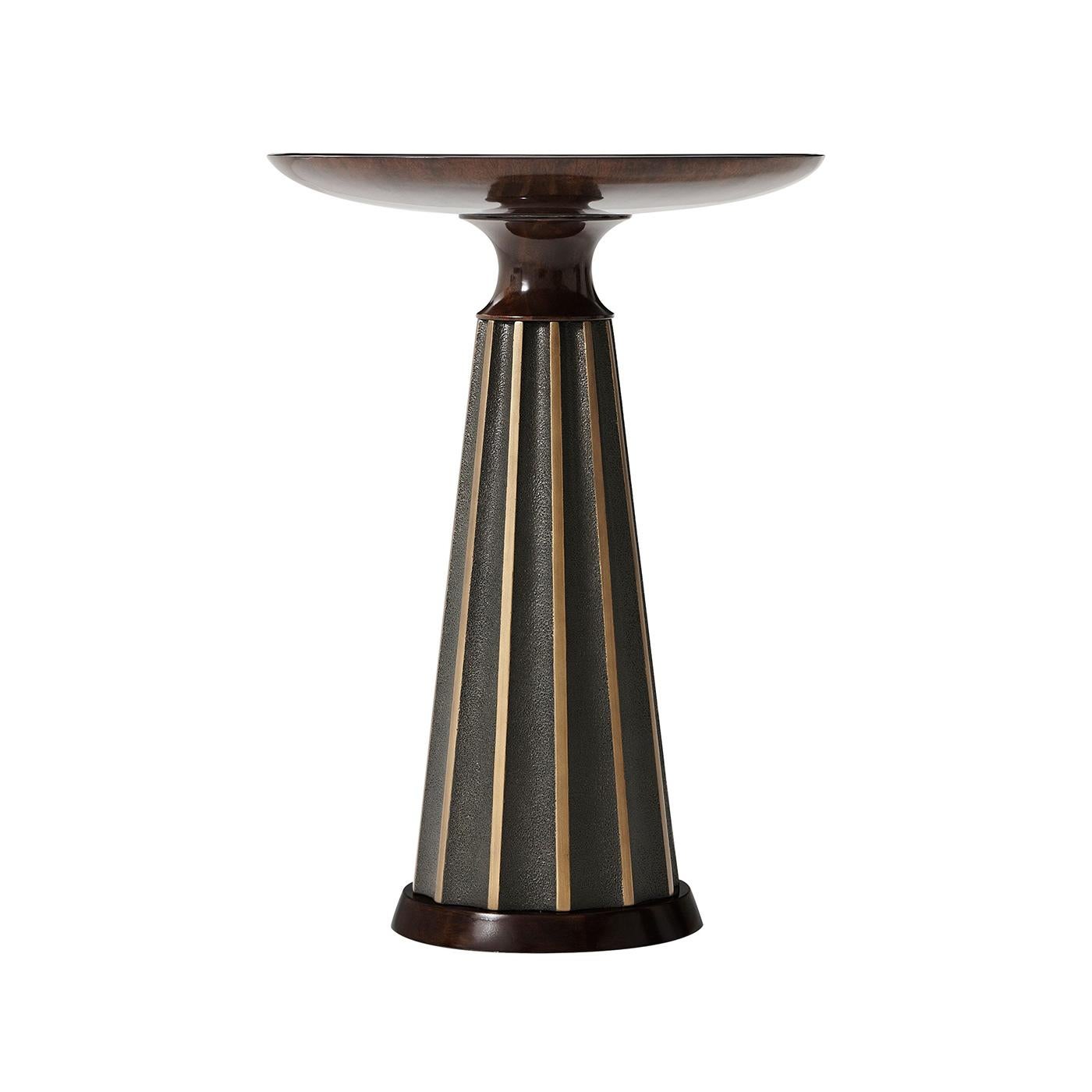 An Art Deco accent table with a polished walnut finish top and base with a figured walnut veneer above a composite tapered radial pedestal base with gilt highlights and textured ground.

Dimensions: 16