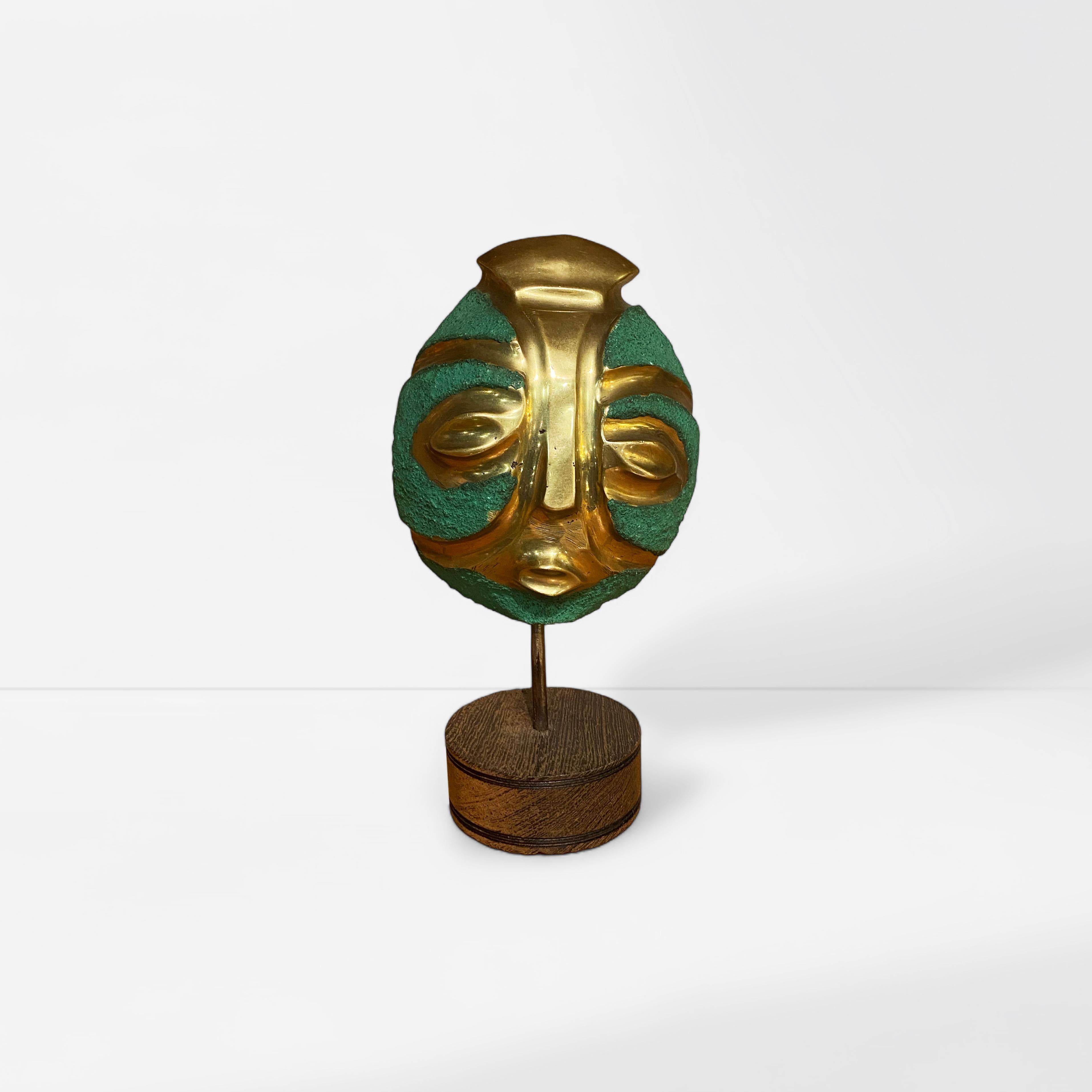 Striking small decorative mask made of brass and treated bronze in verdigris finish with a round hand-curved oak wood base.

Made in the 1960s and represents either an African or a Mayan tribe.. 

Eitherway is a beautiful piece to decorate your desk