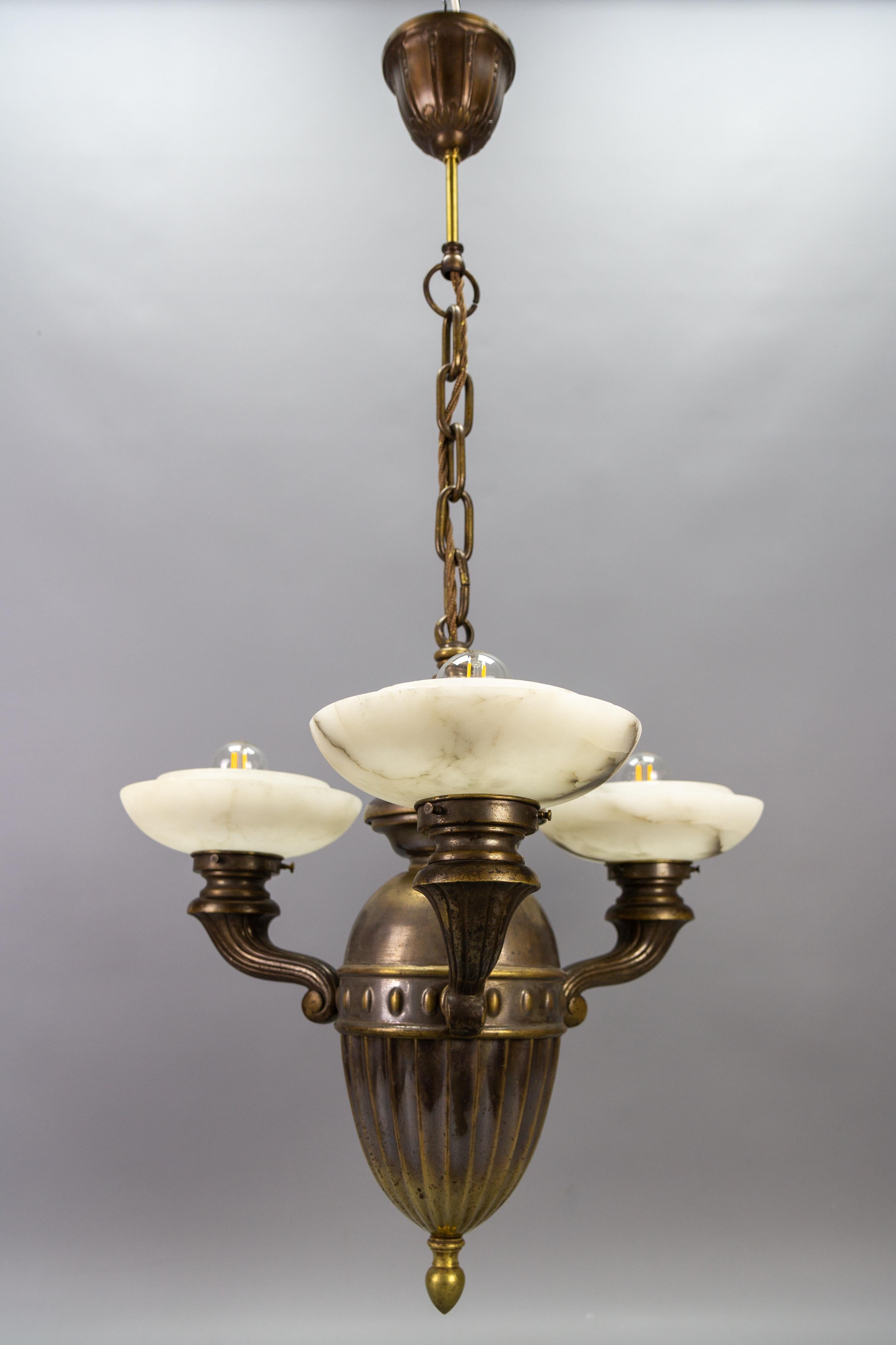 Art Deco alabaster and brass three-light chandelier, 1930s.
This elegant chandelier from the 1930s features a dark brass oviform body with three arms each with a beautiful white and dark veined alabaster shade and a socket for E27 (E26) size light