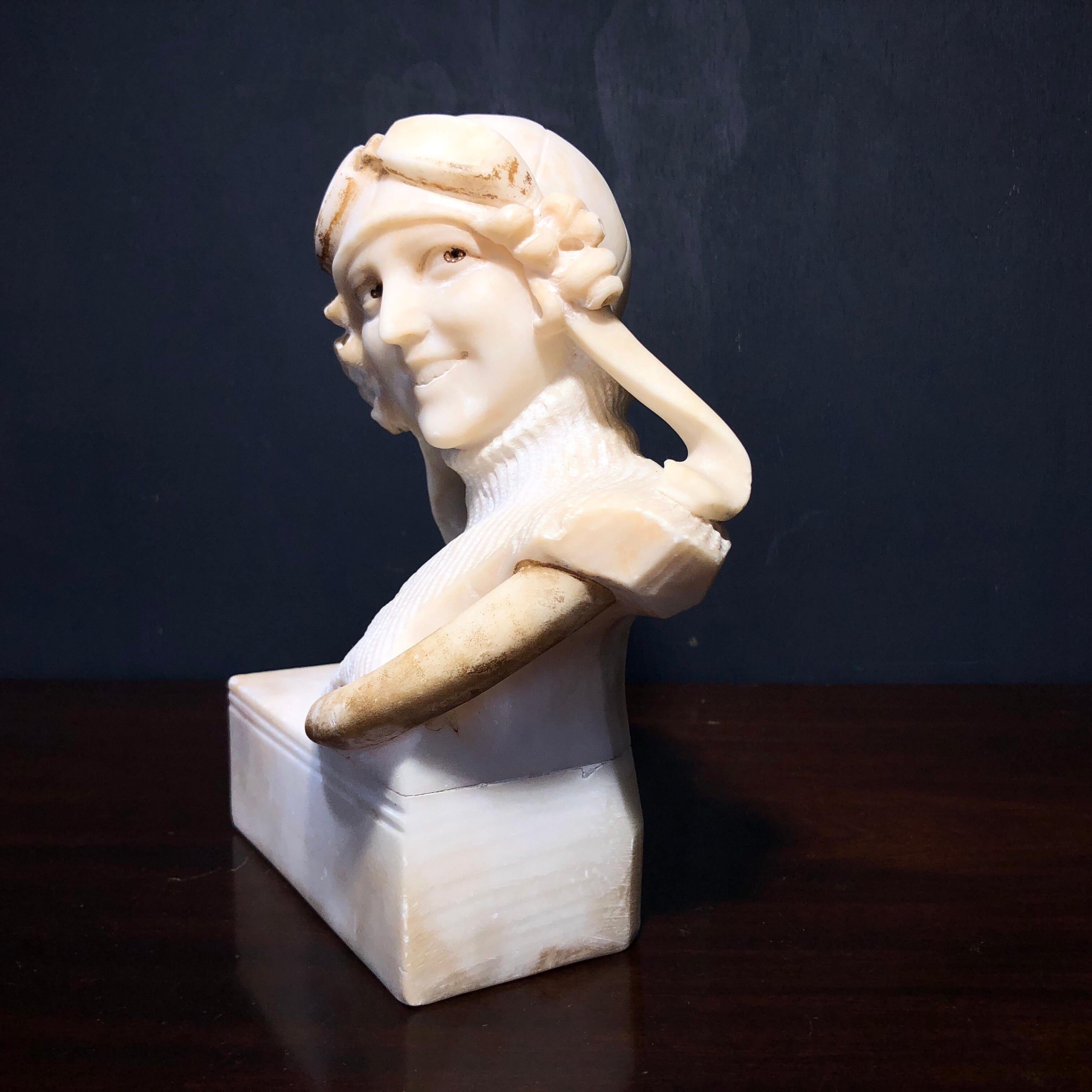 Stylish Art Deco Alabaster bust of a female automobile driver, shown with leather helmet & goggles, in a thick turtleneck sweater, mounted on a rectangular sockle off-center with steering wheel across her front.

signed “Giusto Viti”,

active