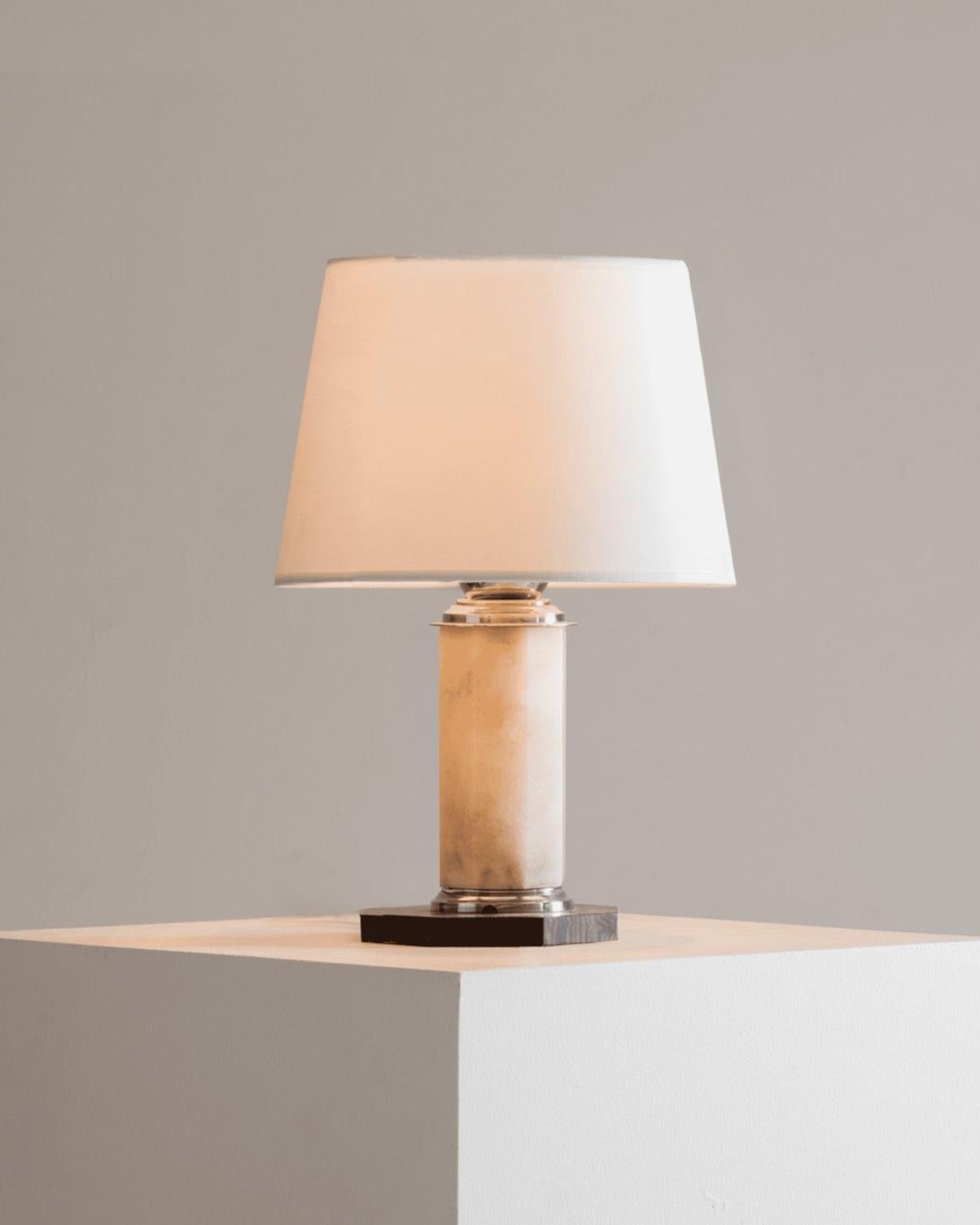 Art Deco lamp base, 1930s, composed of a polished alabaster cylinder, topped and banded with chromed metal fittings.
The octagonal base is made of Macassar ebony. The piece exemplifies the Art Deco aesthetic.
Lampshade not included. Fitted with a
