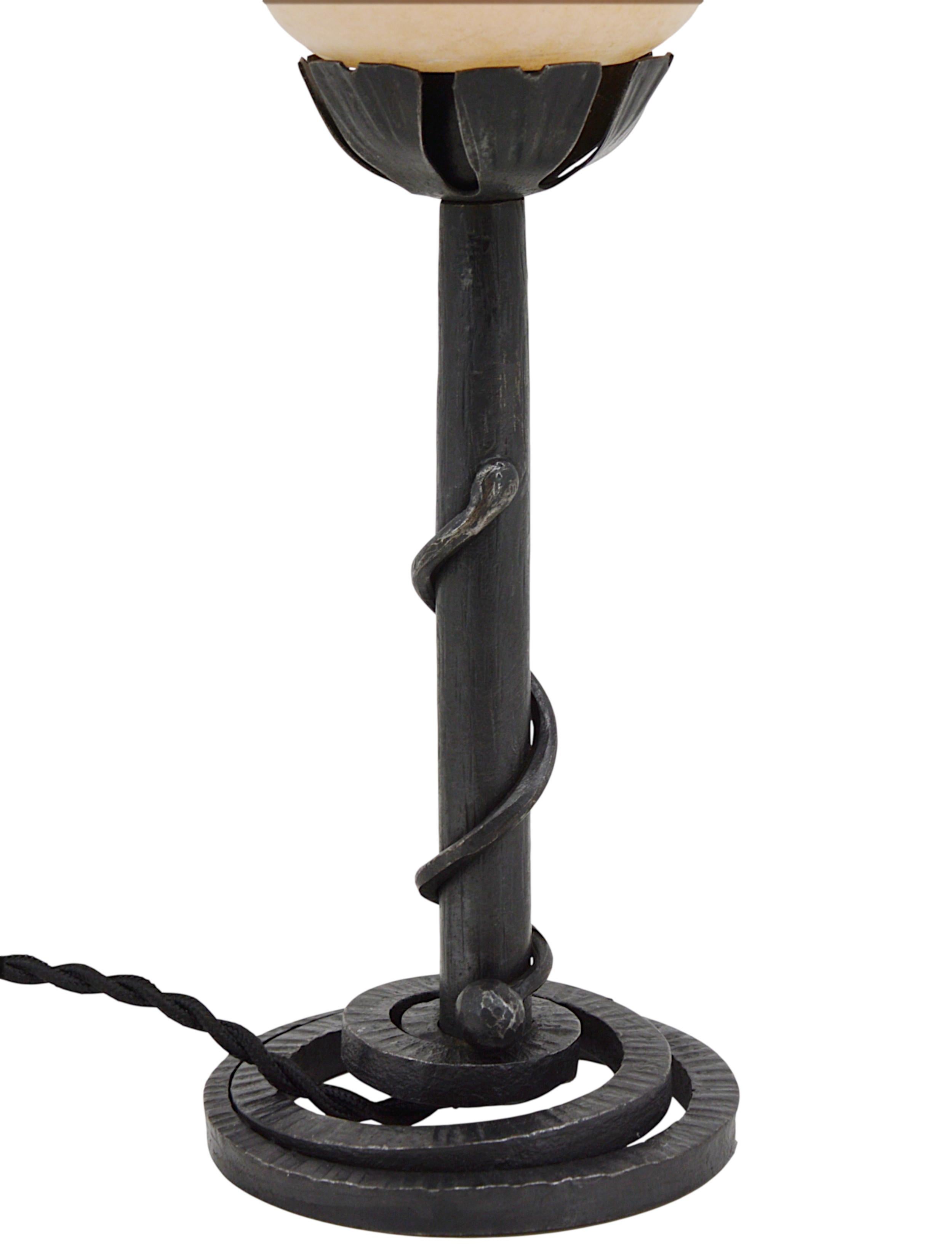 Cette rare et élégante lampe de table Art déco française, datant des années 1920, présente un abat-jour sophistiqué et moderniste en albâtre reposant sur une base en fer forgé conçue pour symboliser un serpent. La base est estampillée 