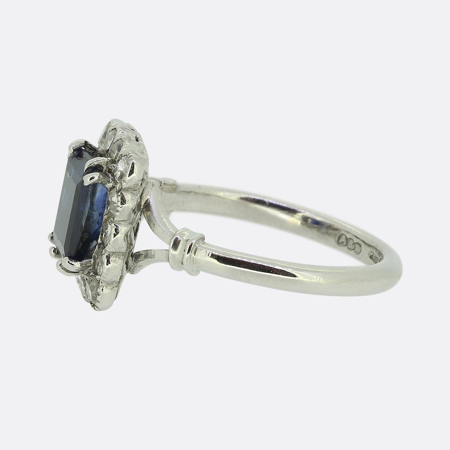 Here we have a wonderful Art Deco sapphire and diamond ring from the manufacturers Alabaster and Wilson. The ring features a mid to dark blue emerald cut sapphire that sits in a raised double claw mount. Surrounding the emerald cut sapphire there