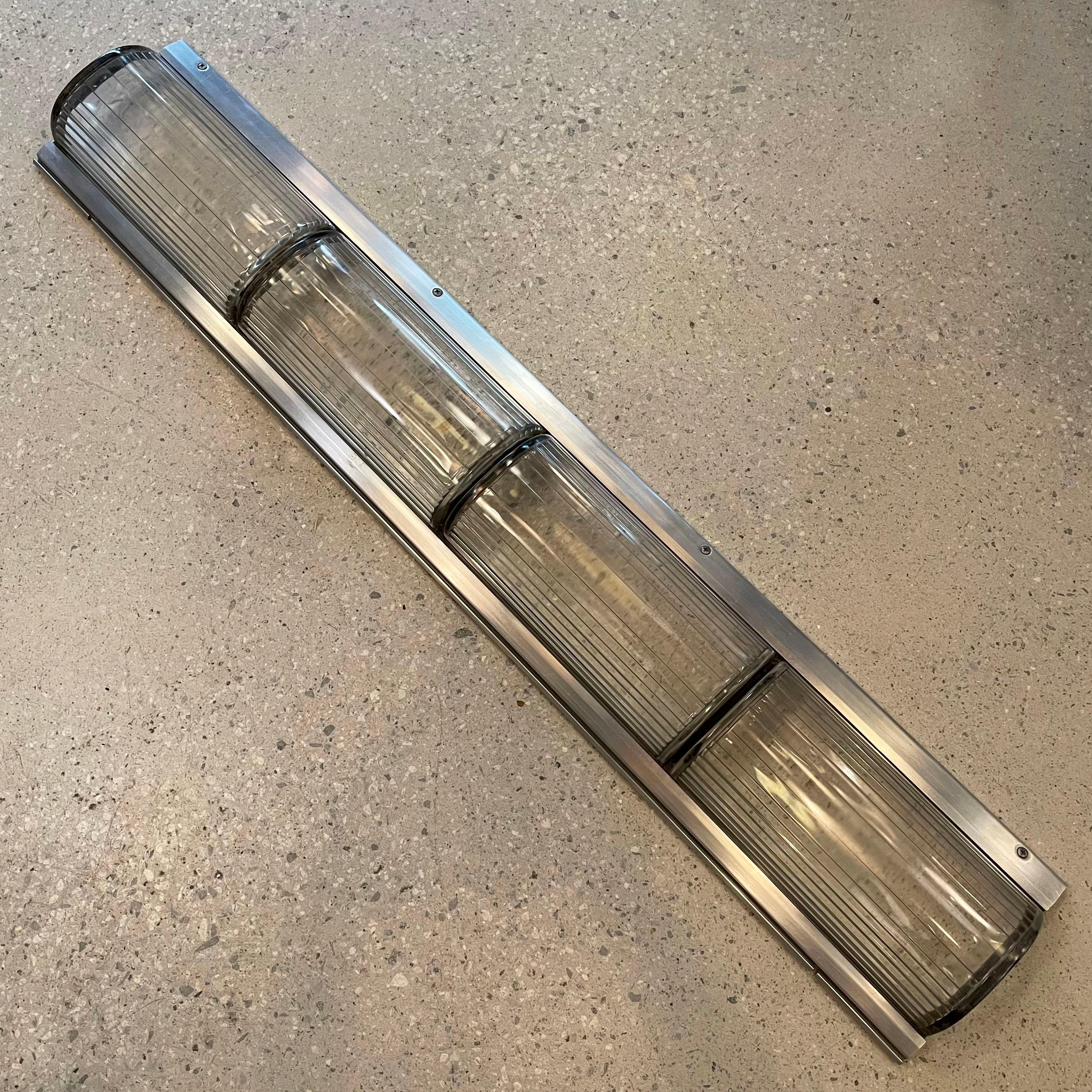 Die architektonisch anmutenden, im Art-Déco-Stil gehaltenen U-Bahn-Leuchten verfügen über einen Aluminium-Rohrrahmen mit gerippten, diffusen Pyrex-Glasschirmen, die durch ein schwarzes Gummiband in 4 Abschnitte von einem Fuß unterteilt sind. Die