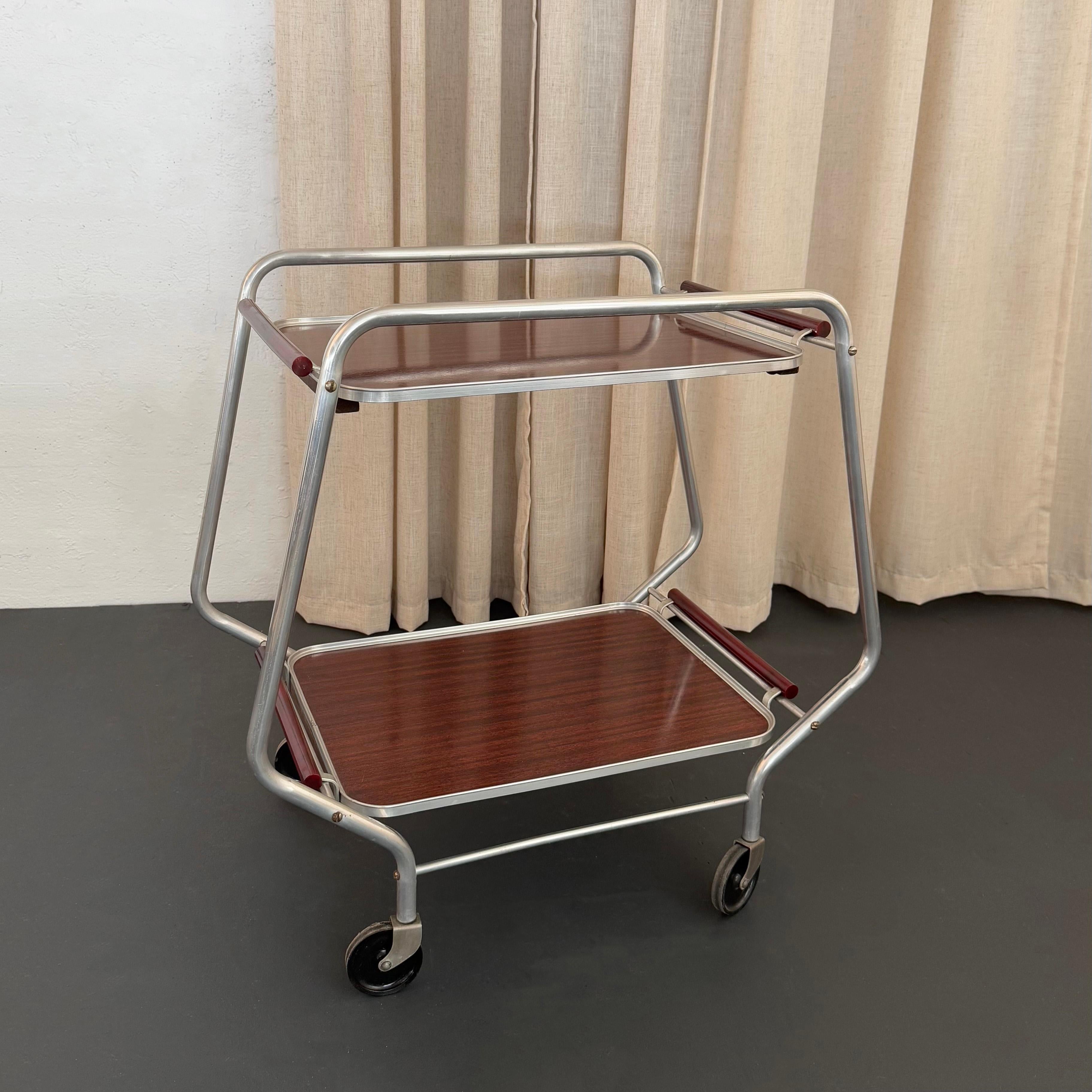 This streamlined Art Deco bar cart / serving trolley is a wonderfully elegant and highly functional piece. The cart features a tubular aluminum frame in a rounded hexagon shape that rolls smoothly on casters. It has two tiers with removable formica