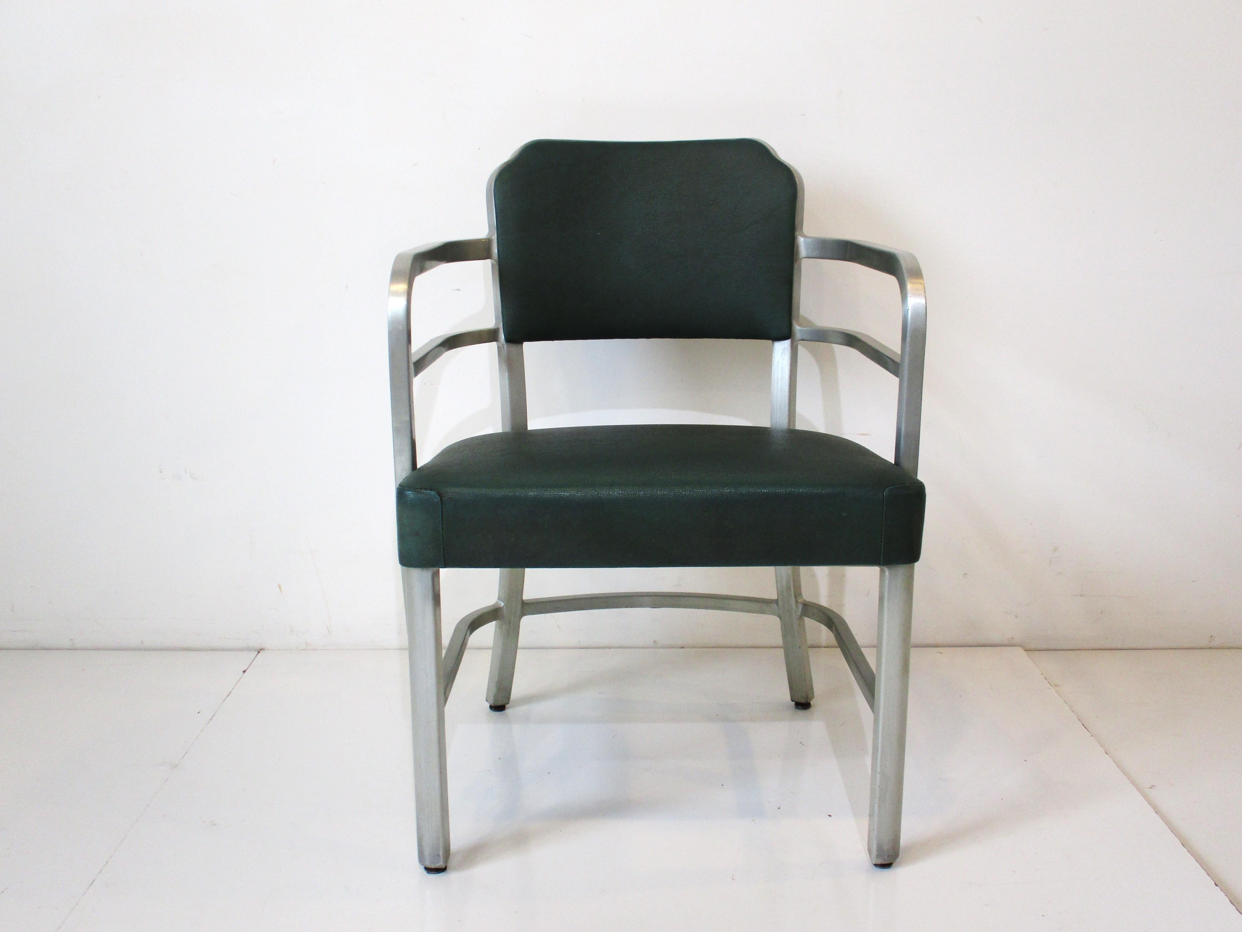 A brushed aluminum framed armchair with curved arm rests and upholstered seat and back. The fabric is a textured dark greenish leatherette and came from the barber shop at Cincinnati's inconic Union Terminal Art Deco train station. Manufactured by