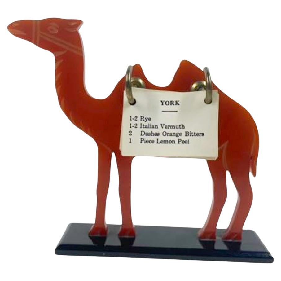 Art Deco amber Bakelite cocktail recipe stand. A camel silhouette in amber Bakelite standing on a black Bakelite foot and having a pair of hooks holding a selection of flip cards with recipe for making cocktails. 