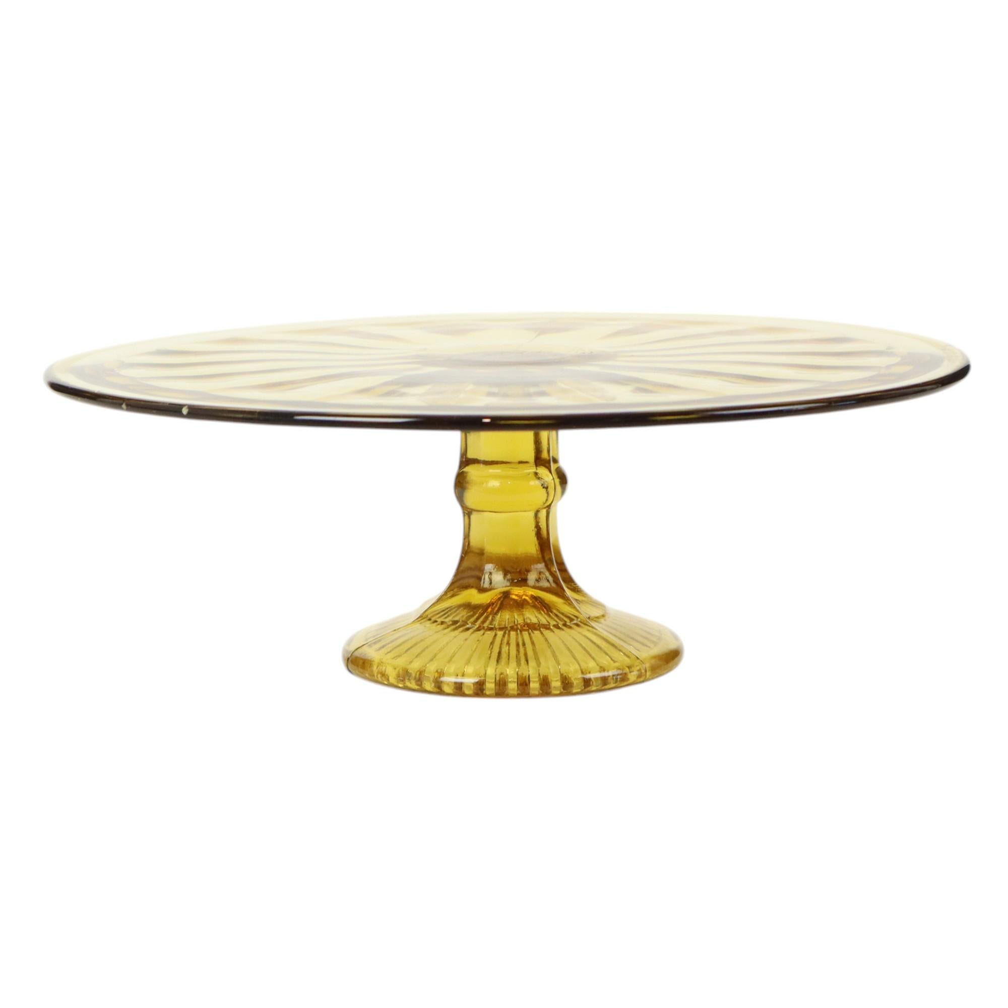 Alzata per torte art déco color ambra, piatto rotondo per torte con motivo decorativo e piede, realizzato in vetro pressato, chiamato anche vetro a depressione, il design è attribuito alla vetreria belga Verrerie de Scailmont, prodotto tra il