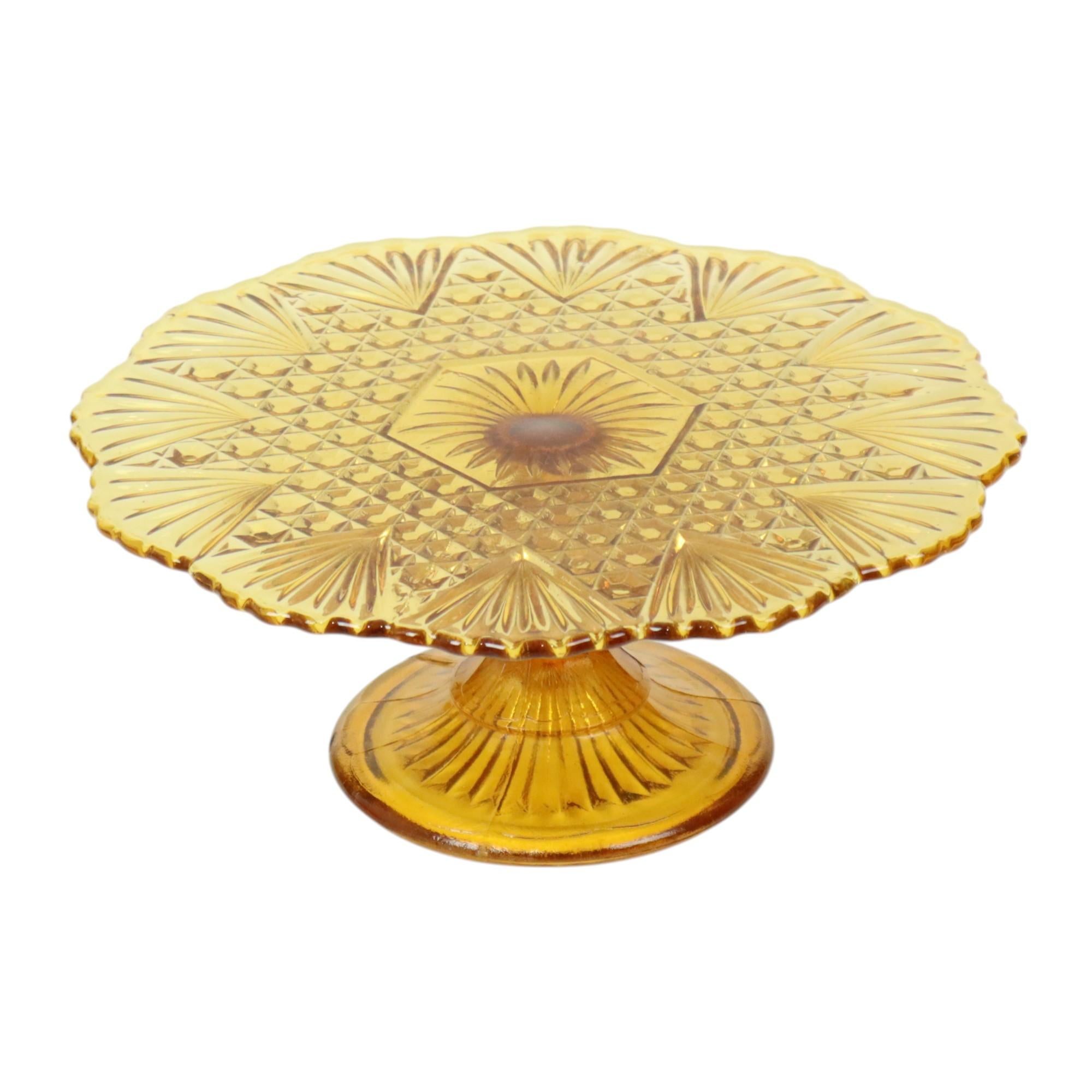 A beautiful, large vintage amber-colored cake stand with a floral and diamond pattern, featuring an elegantly wavy edge along the outside. It is made of pressed colored glass, also known as Depression glass, from the Art Deco period, and is marked