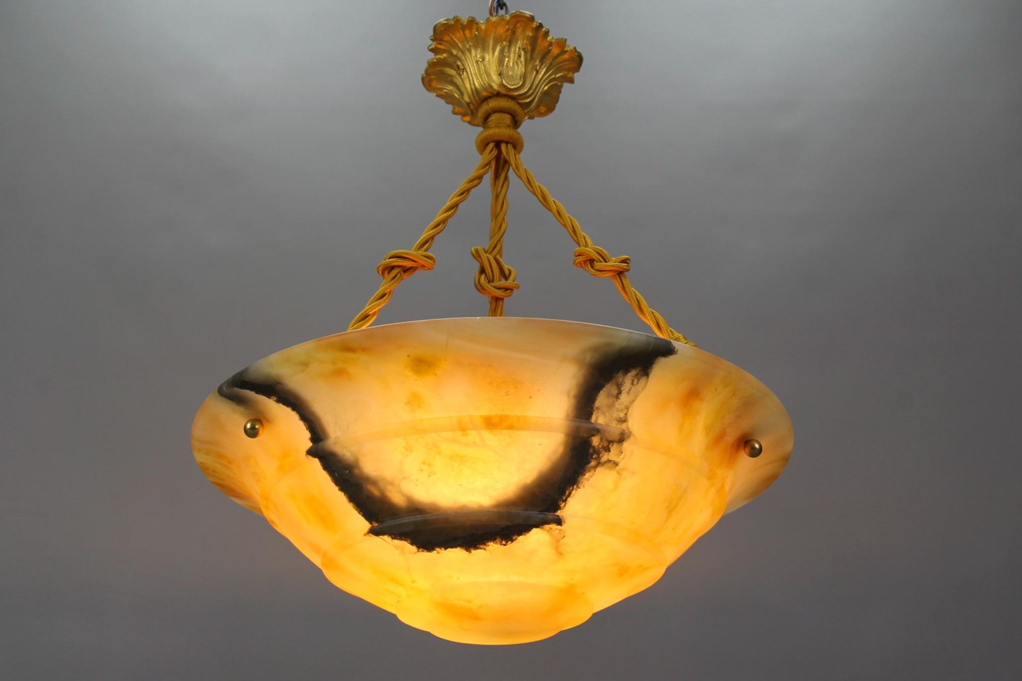 A magnificent Art Deco amber color alabaster pendant ceiling light fixture with black veins. Germany, circa the 1930s. 
This masterfully carved, layered, and beautifully veined alabaster bowl in amber tones is suspended by three ropes (wires) and a