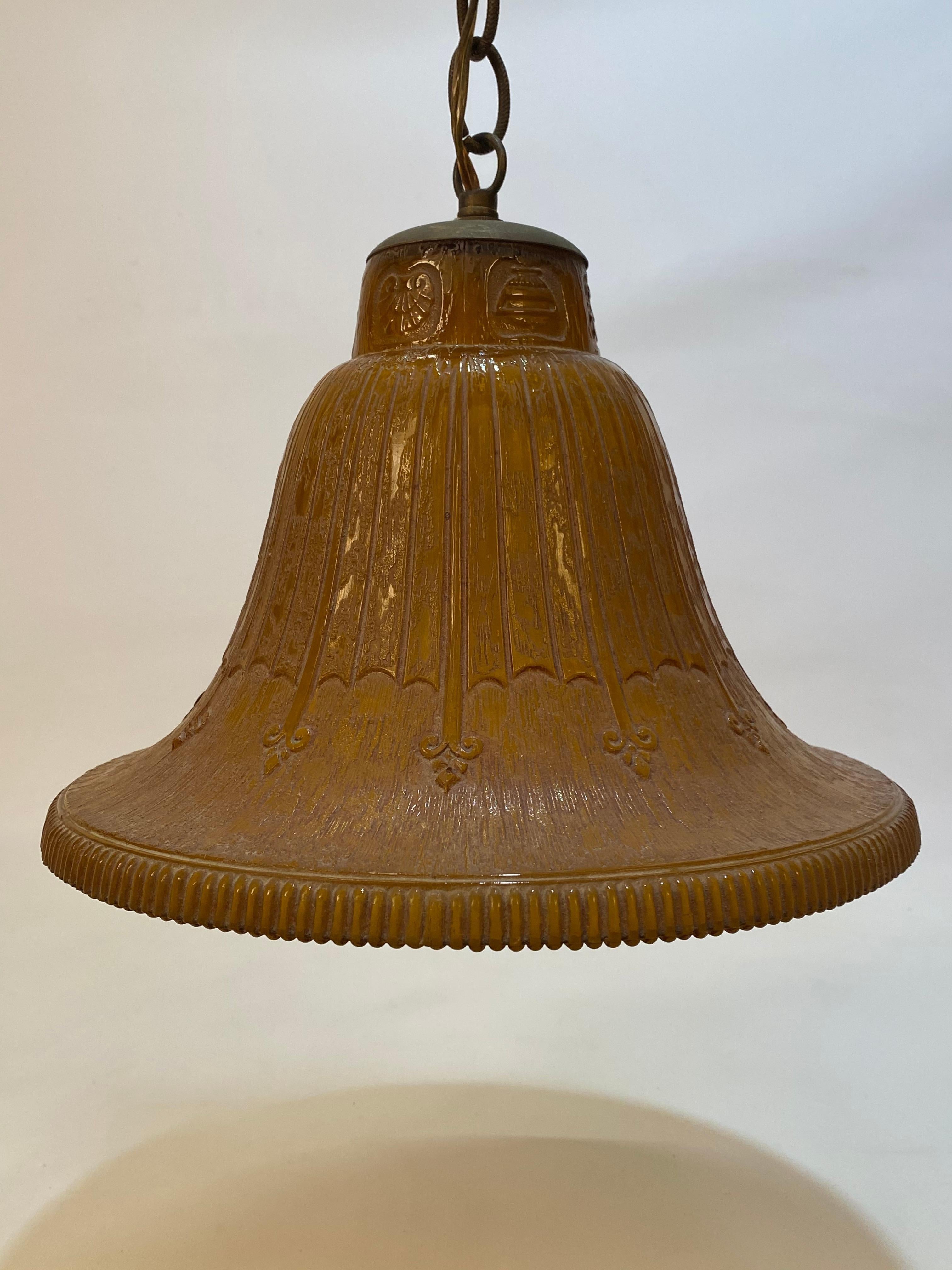 Art Deco period amber glass bell pendant light. Cast mold glass shade decorated with a spade and ribbon design. Ribbed edge. The shade is in very good condition with one minor ding to the edge (very difficult to see).

Measures: Approximately