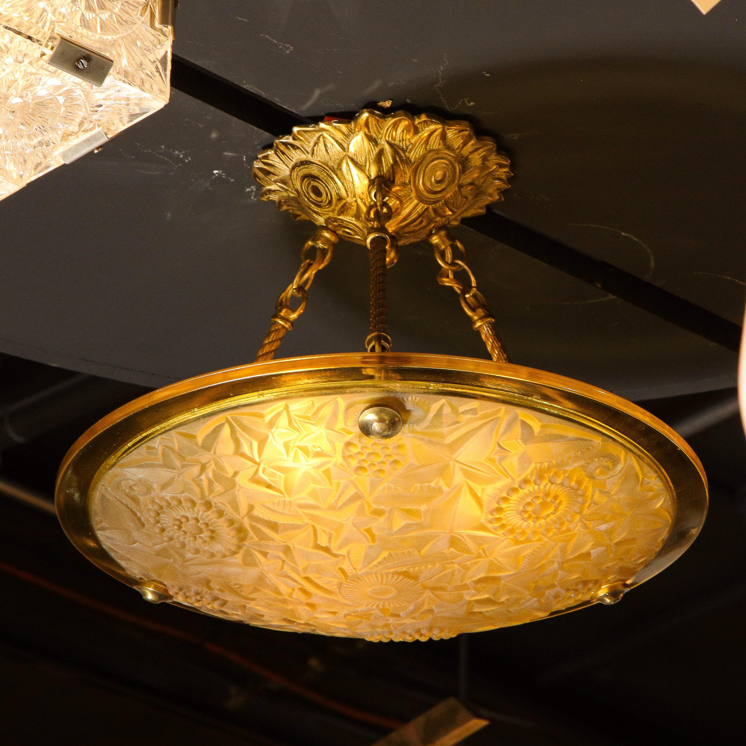 This stunning Art Deco pendant was realized in France circa 1930. It features a circular domed amber shade with a wealth of etched foliate and geometric cubist motifs- including stylized maple leaves- secured by gilded bronze fittings. The