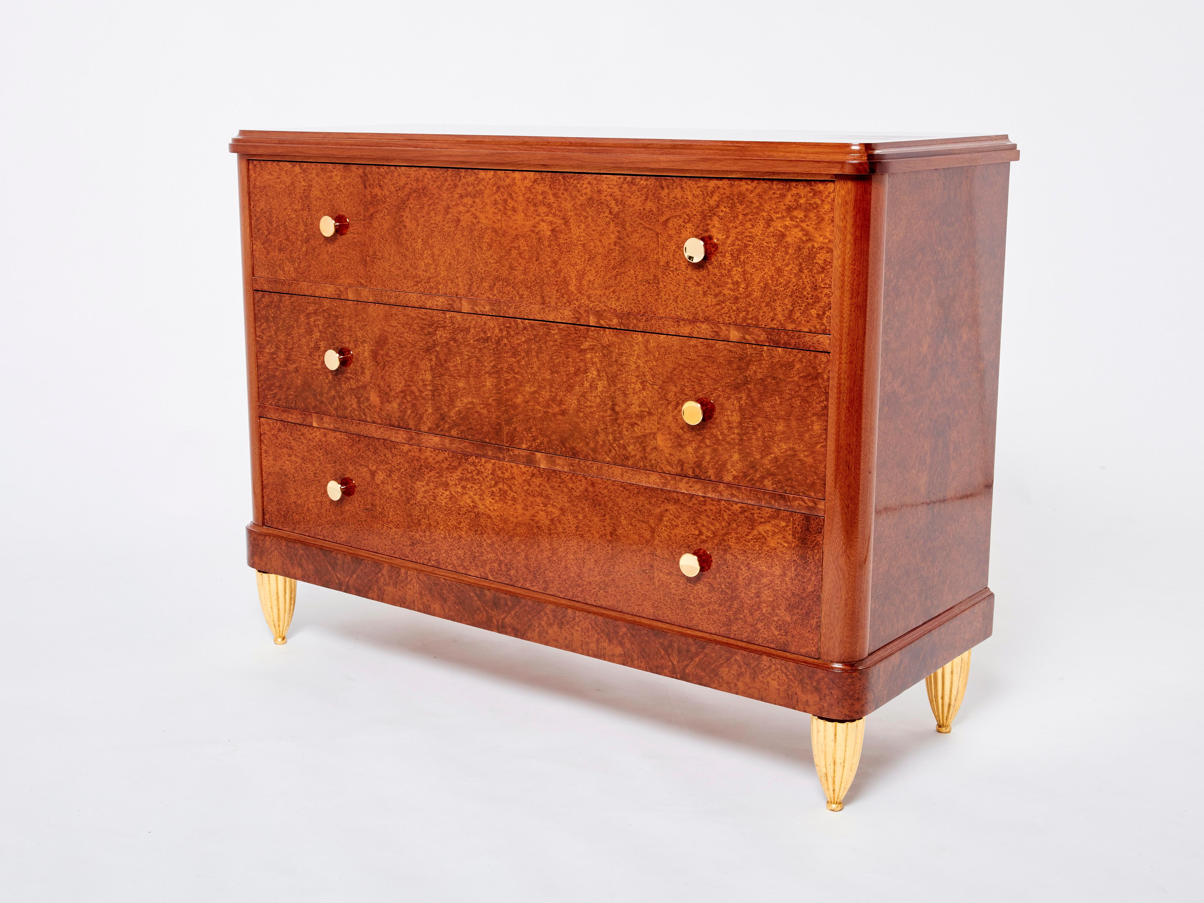This beautiful 1940s Art Deco chest of drawers attributed to Maurice Dufrène imparts a cosy, glowing mood to any space. The warm amboyna burl wood remains looking healthy and smooth some eighty years later. Gilded carved feet and solid brass handles