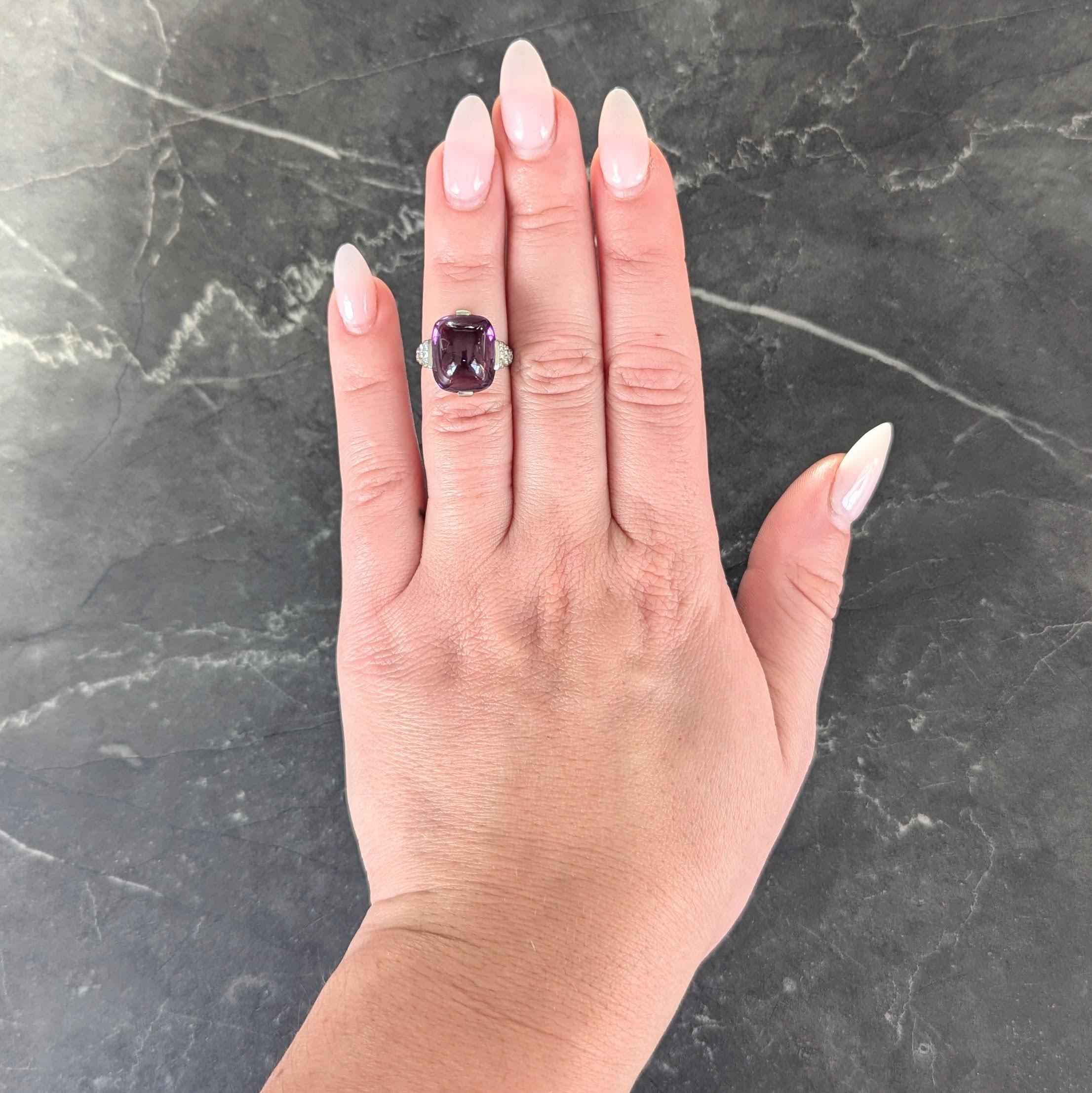Centering a sugarloaf shaped amethyst cabochon measuring 11.0 x 13.5 mm
Transparent medium purple in color with natural black speckle inclusions
Set with wide tab-like prongs and flanked by stepped shoulders
Bead set with single cut diamonds with