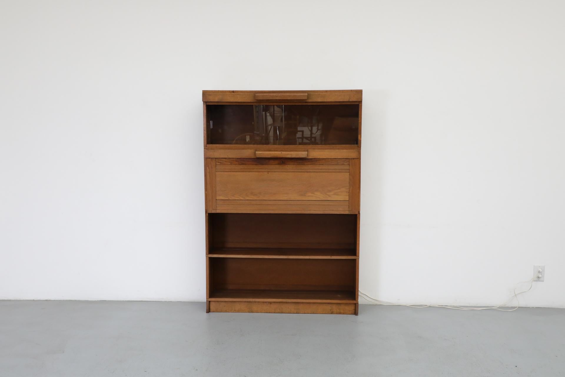 Art Deco - Amsterdam School wide dark oak stacked storage cabinet with many stylish and  components. This piece, similar to a barristers bookcase features sliding glass doors, a drop down desk or bar (with glass surface), and 2 units of full width