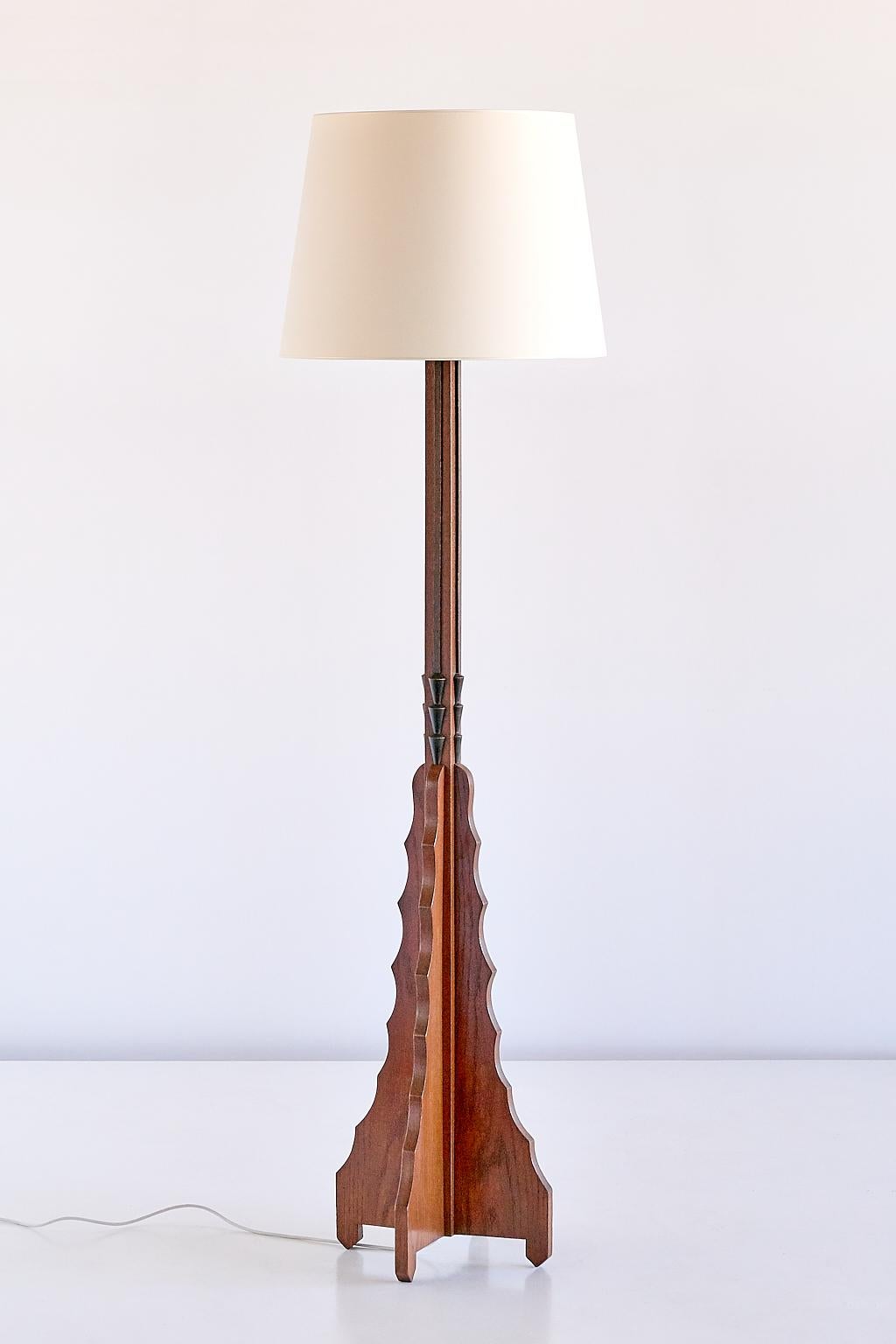 This striking floor lamp was produced in The Netherlands in the early 1930s. The frame in solid and stained oak is defined by the tiered base with an intricately carved pattern. Each side of the middle part of the lamp foot is accentuated by a